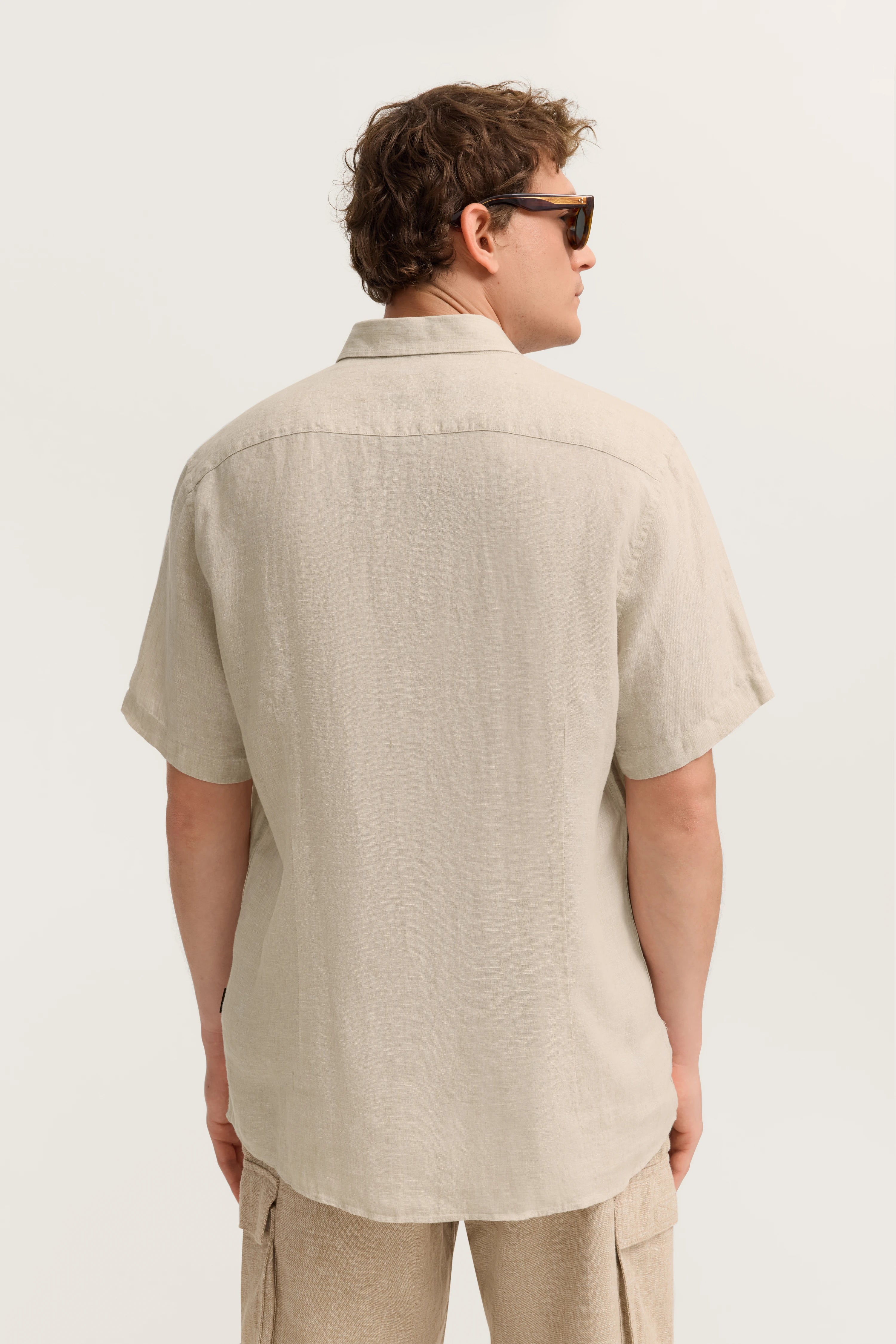 Beigefarbenes Hemd und Shorts in Leinenoptik, Model von hinten, lässige Pose, bugatti Stil.