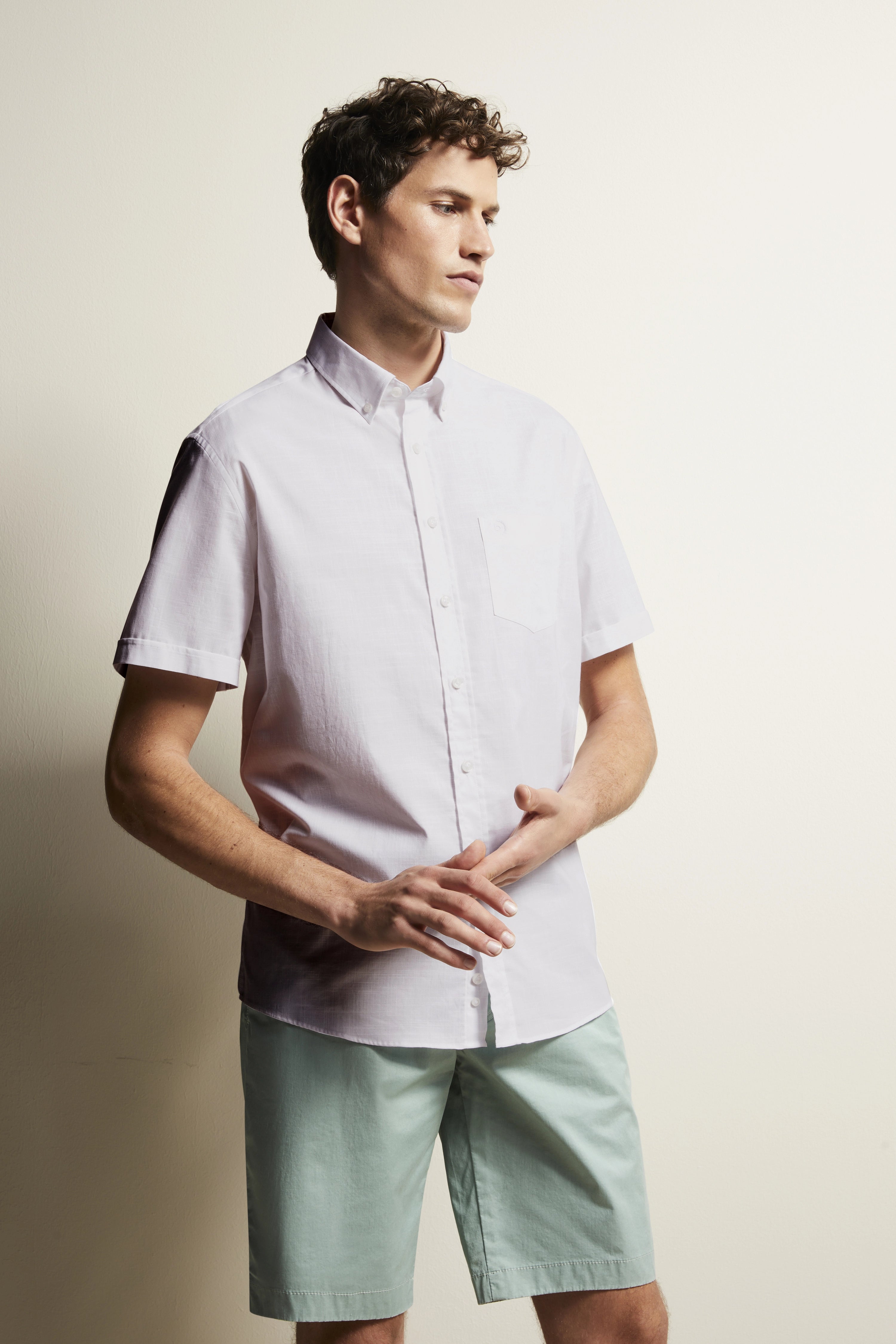 Model in wit overhemd en mintgroene shorts, zijwaarts poserend, bugatti-stijl.