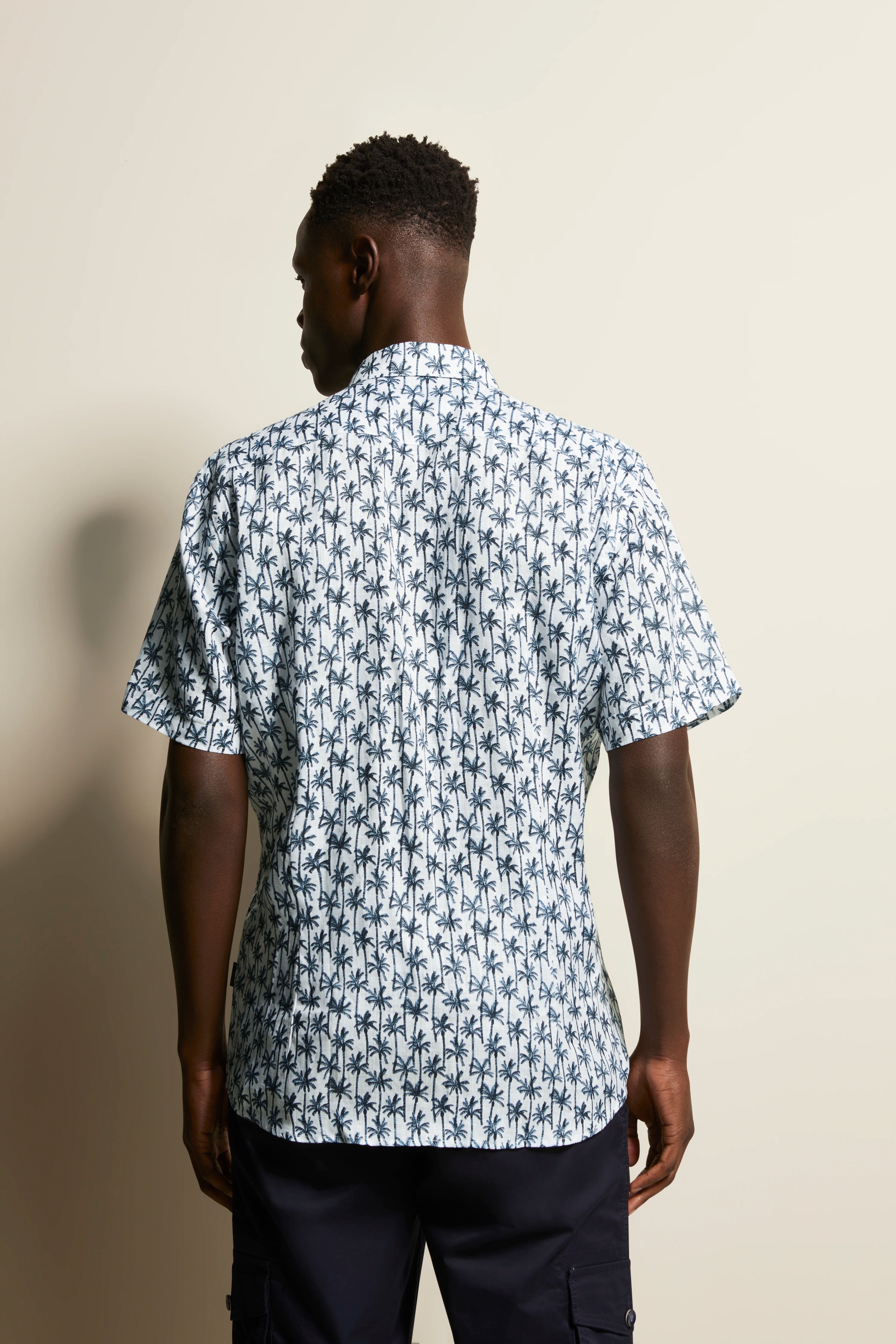 Model, achterkant: Korte mouw shirt met palmmotief in wit en blauw, ontspannen houding.