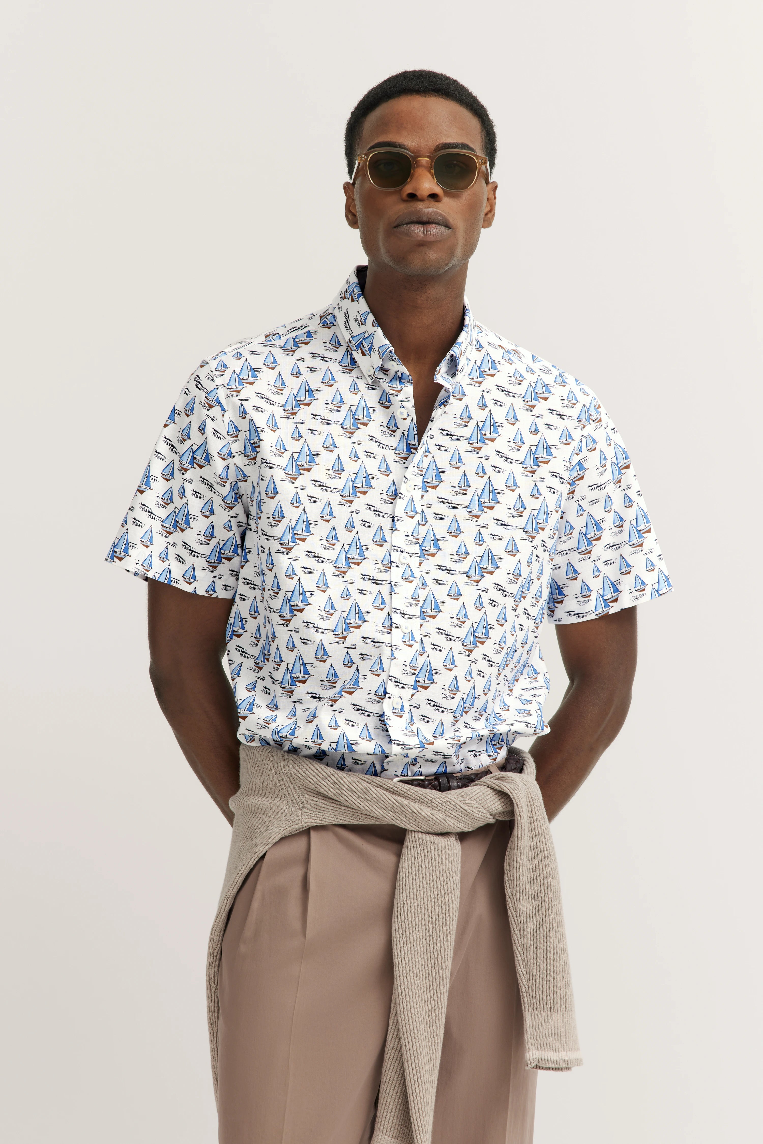 Wit overhemd met blauwe zeilboten, beige trui, beige broek. Modelpose, casual uitstraling.