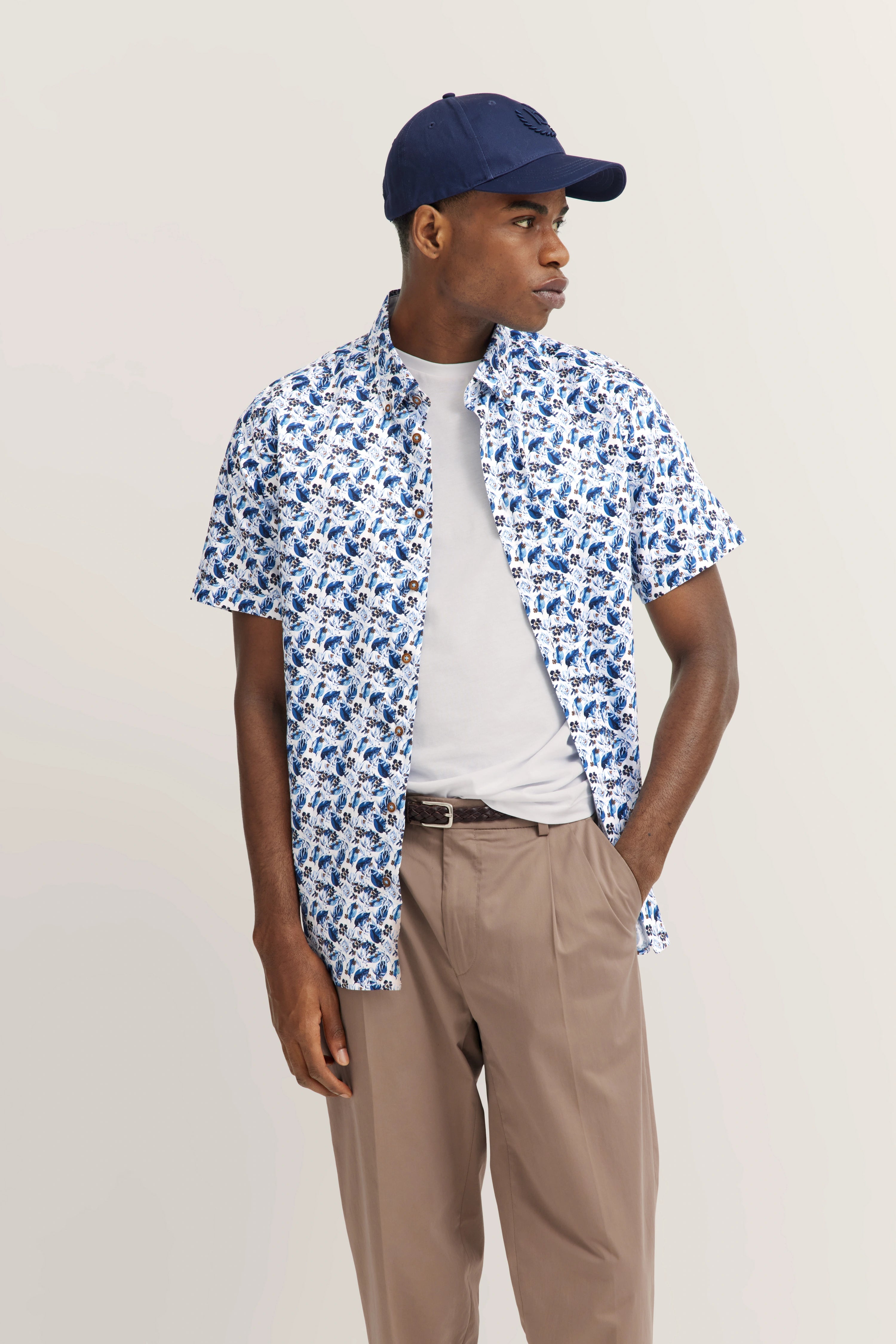 Kortemouw shirt met blauw patroon, wit shirt, beige broek, marineblauwe pet van bugatti.