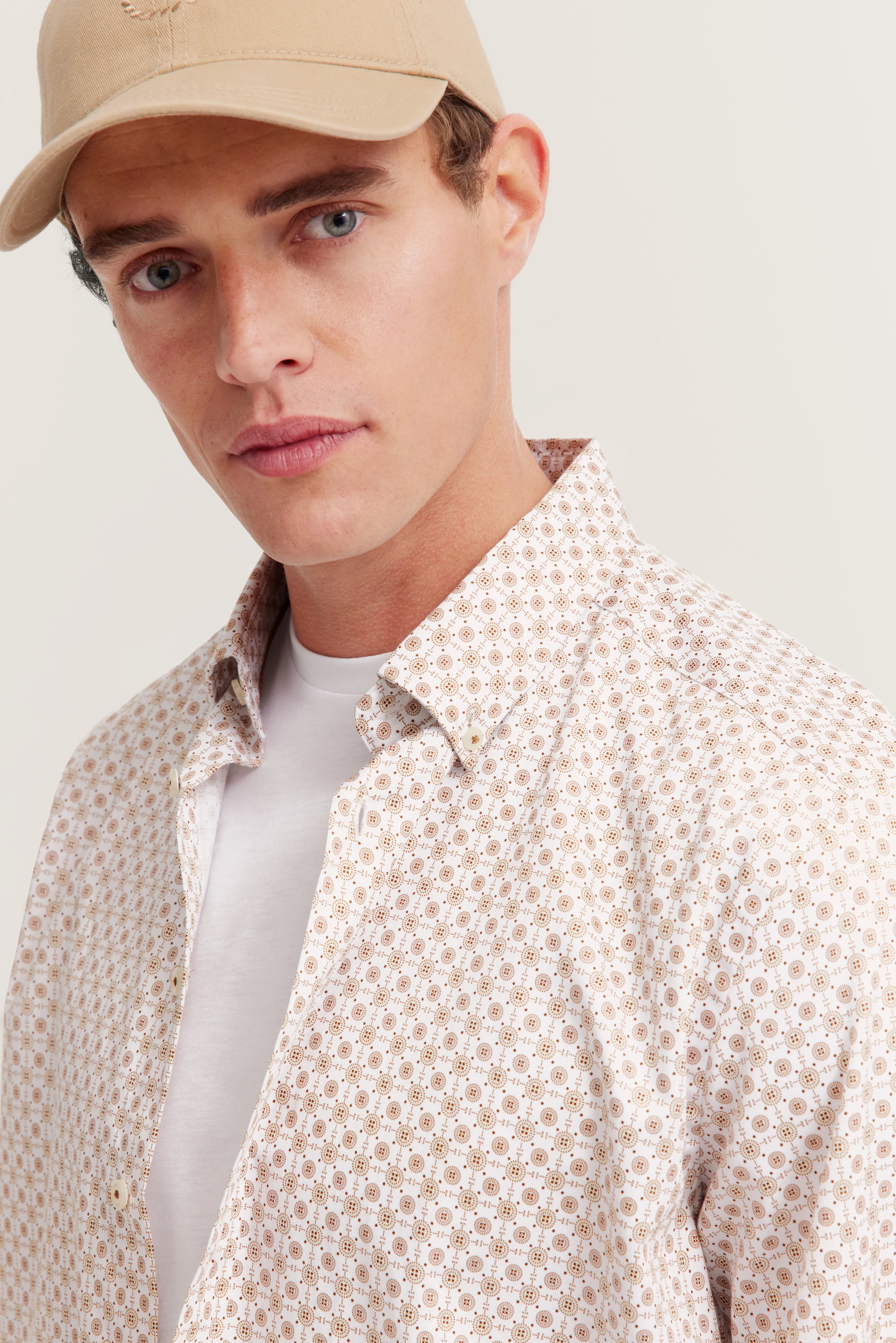 Model met bugatti overhemd met geometrisch patroon in wit en beige, casual pose met beige pet.