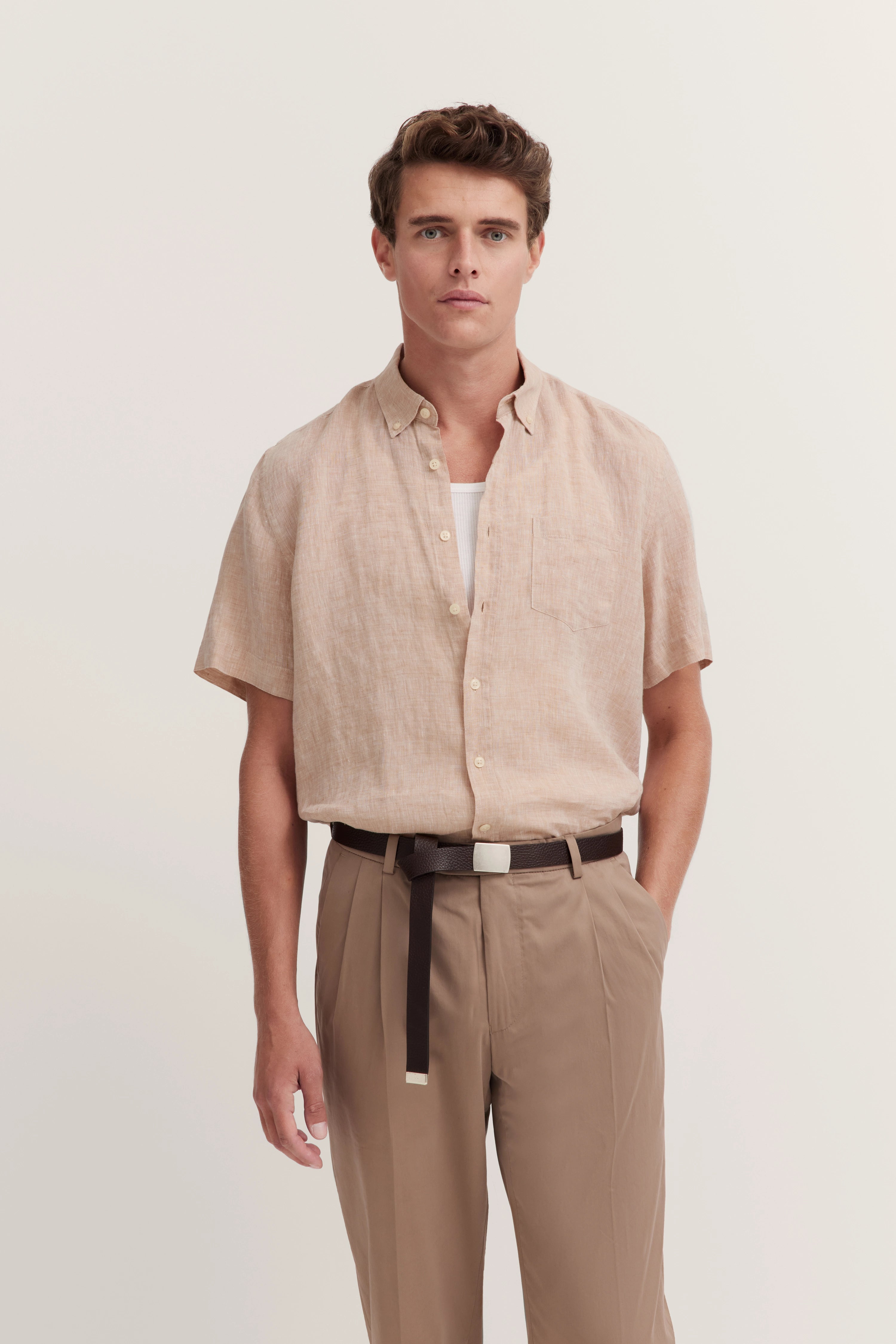 Model in beige kortem mouwenshirt en bruine broek, casual, met ontspannen uitstraling.