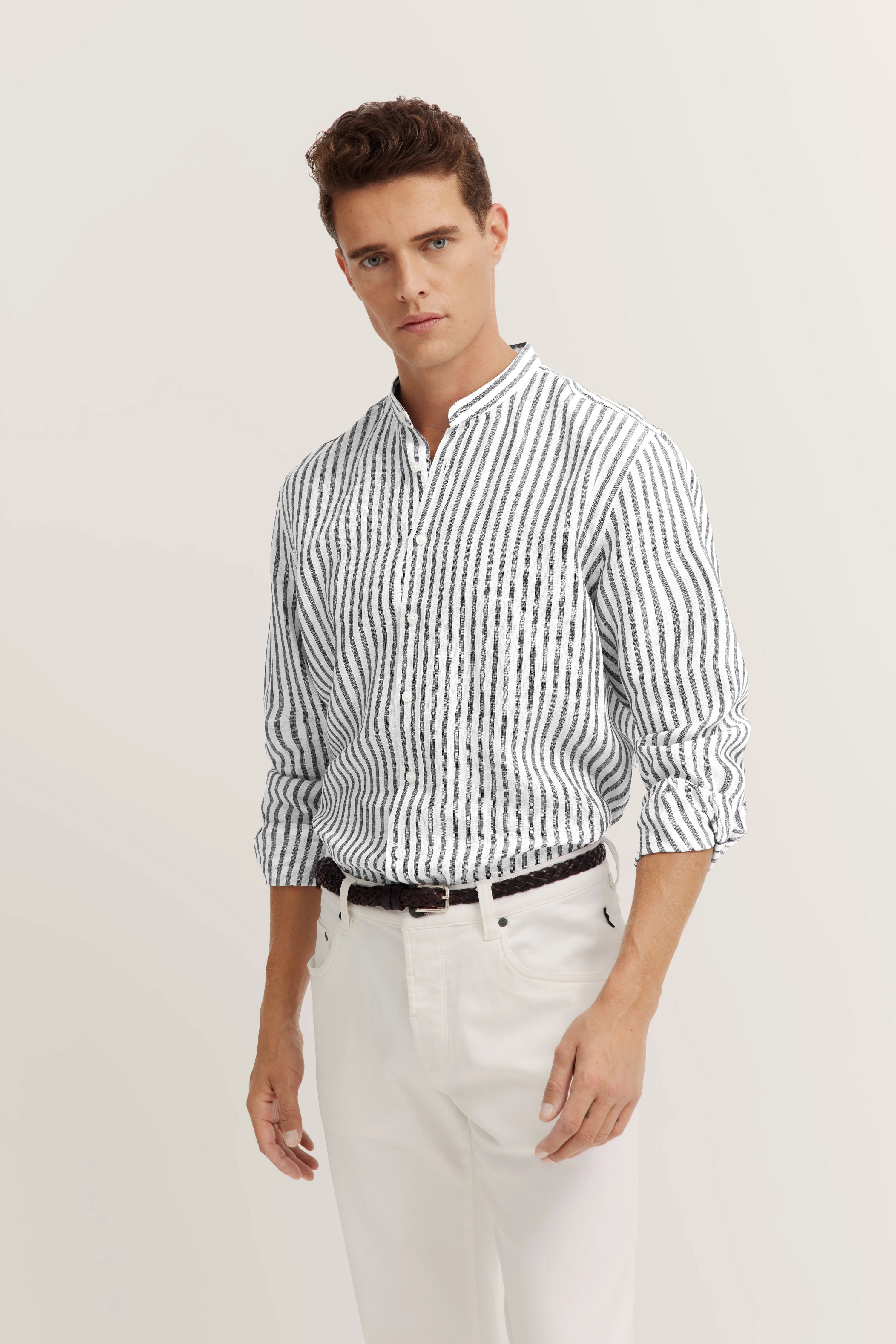 Model in gestreept wit-zwart bugatti overhemd, witte broek, ontspannen houding.