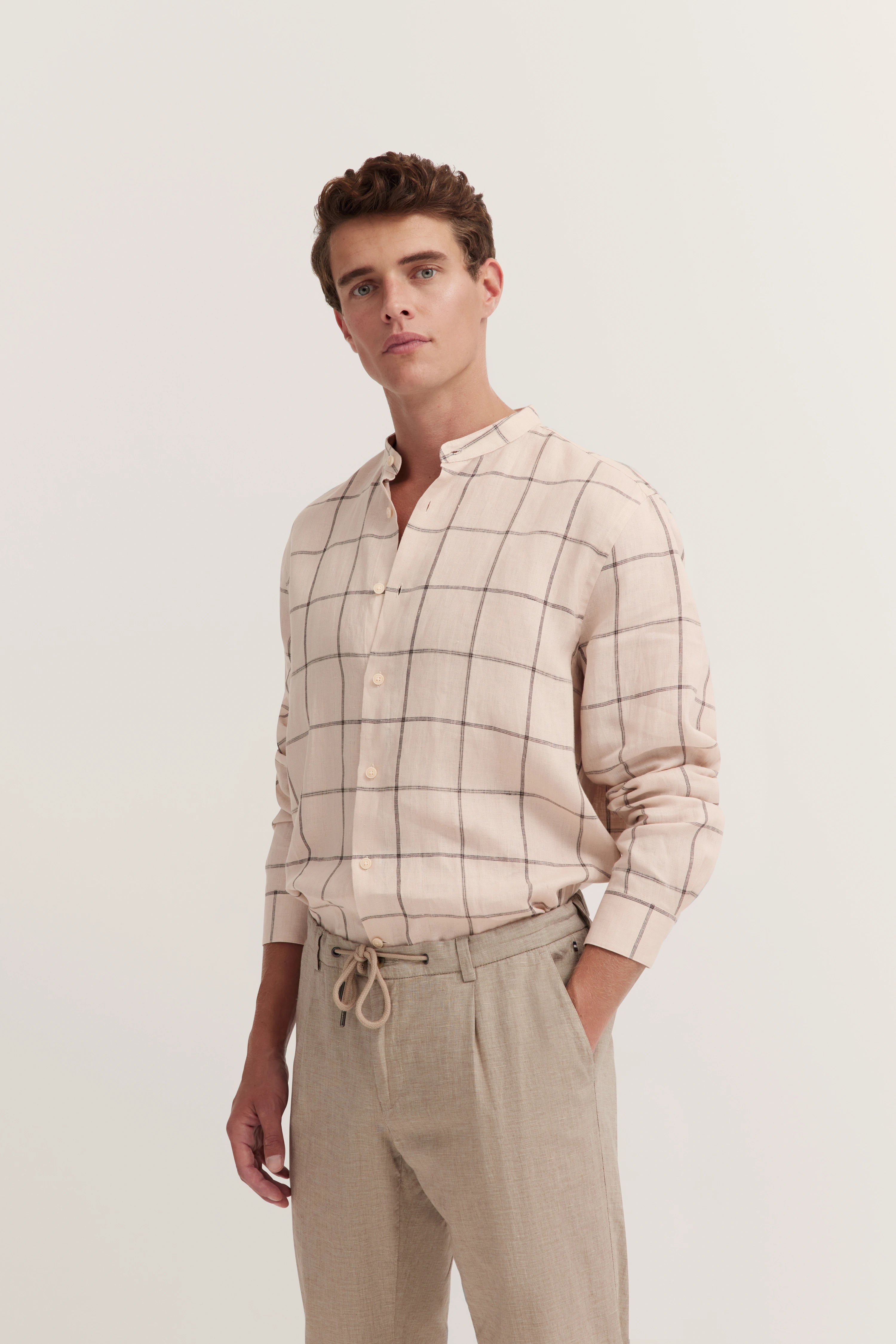 Beige geruit overhemd en beige broek, model poseert ontspannen.
