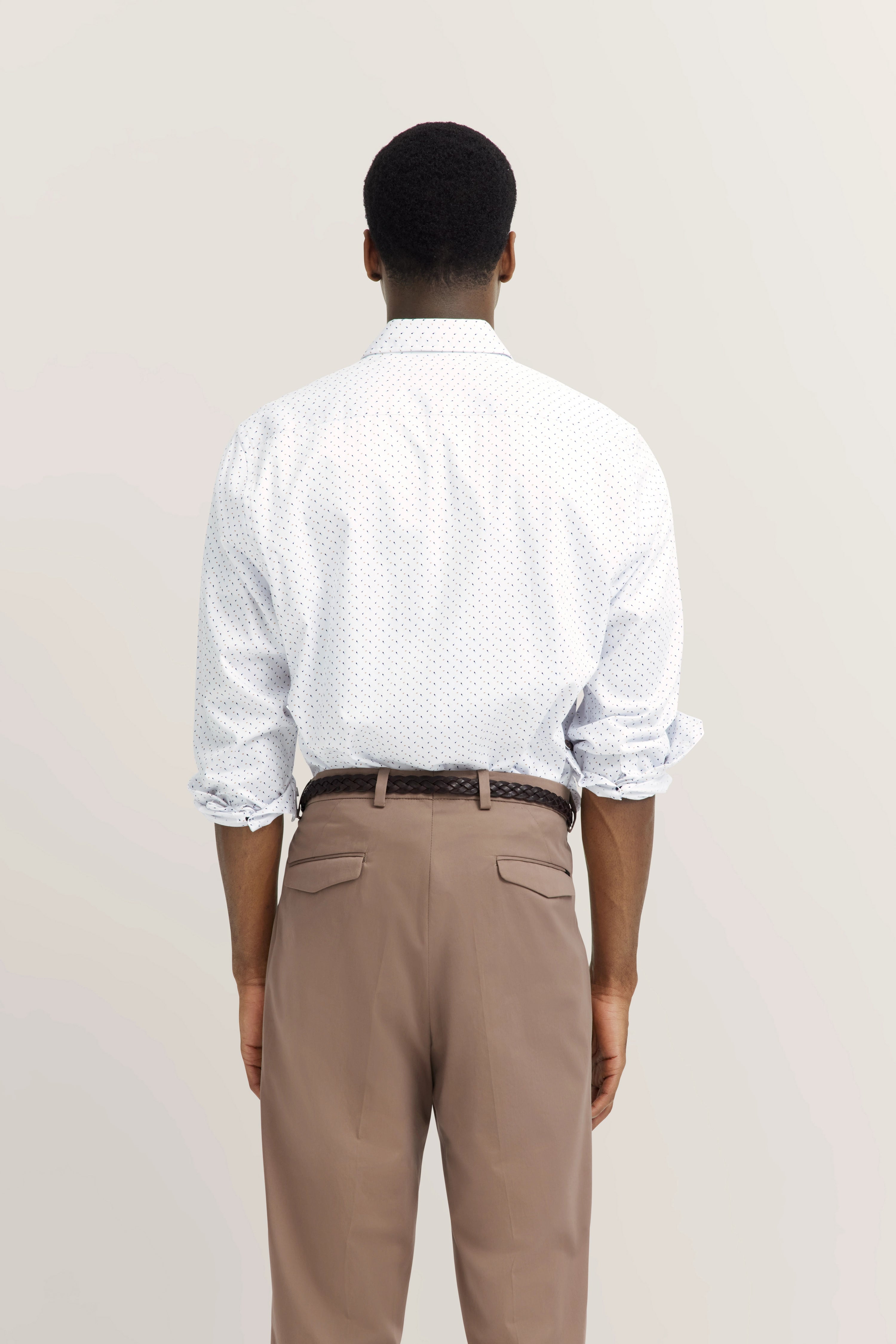Rugaanzicht model in wit overhemd met patroon, beige broek. Opgerolde mouwen.
