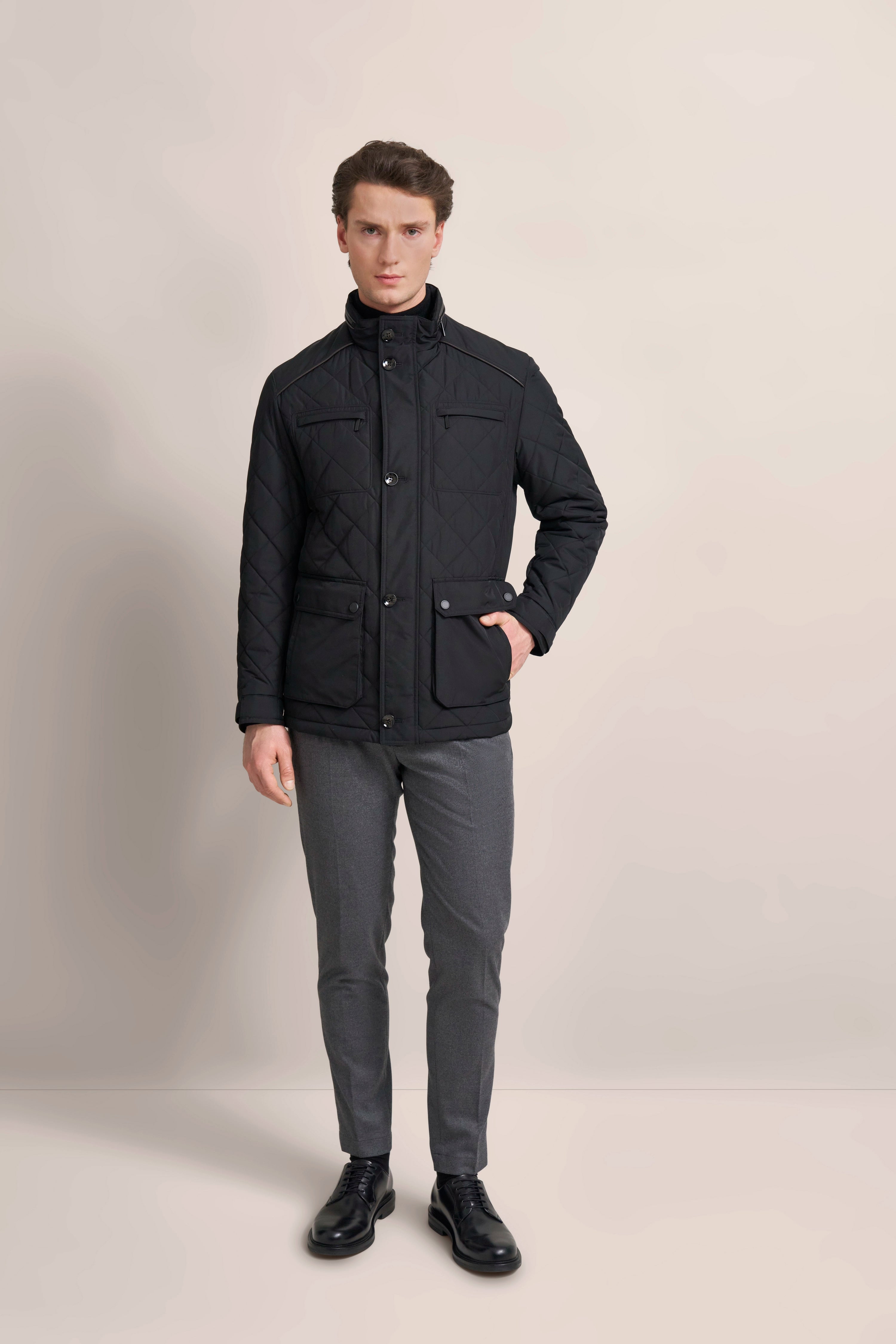 Model trägt schwarze Steppjacke und graue Hose von bugatti, steht aufrecht, Hände in den Taschen.