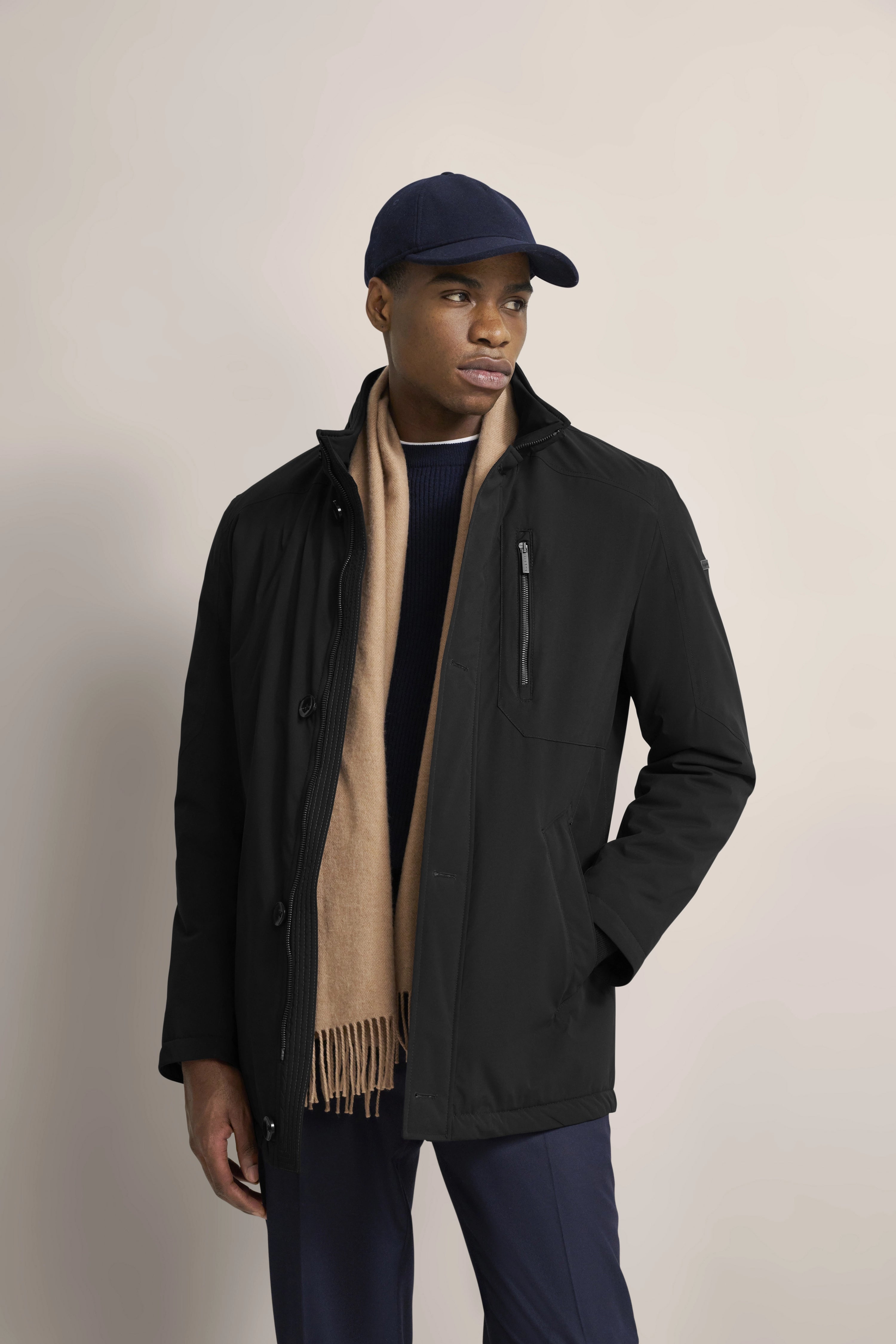 Schwarze Jacke, beiger Schal, dunkelblaue Mütze und Hose