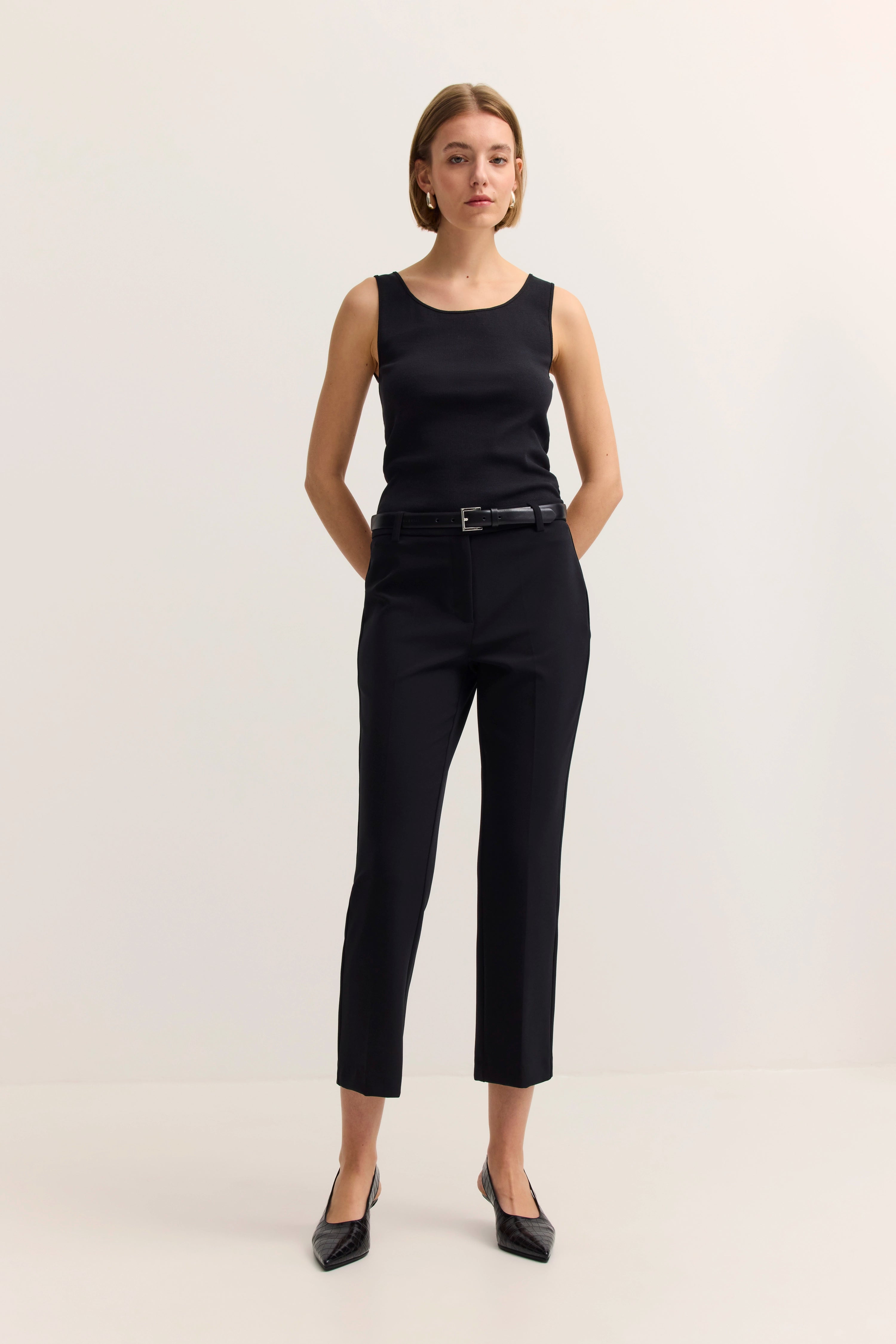 Schwarzes ärmelloses Top und Hose, Model stehend mit Händen in Taschen.