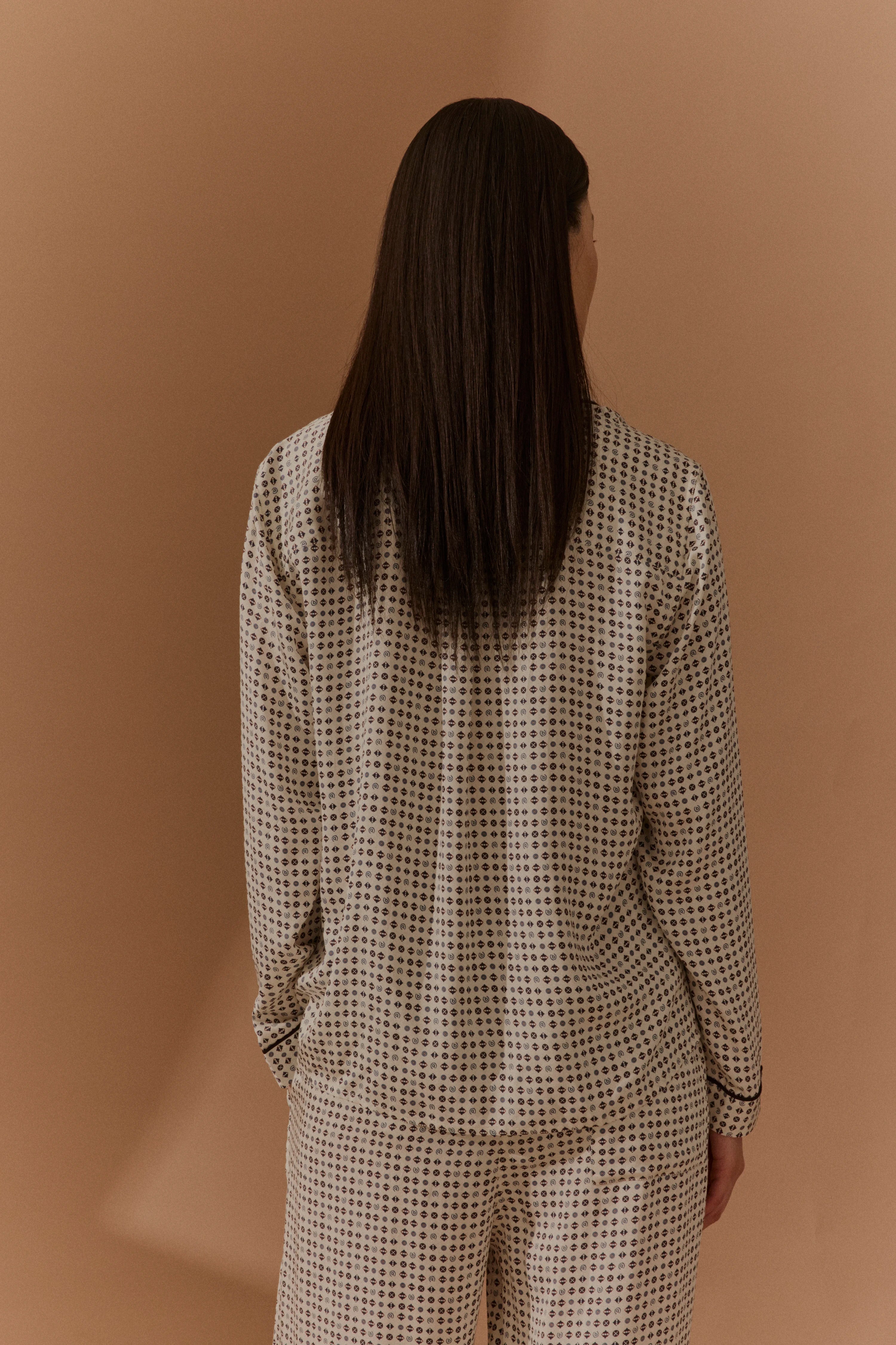 Rückansicht: Model in gemustertem, langärmligem Pyjama-Set in Beige und Schwarz.