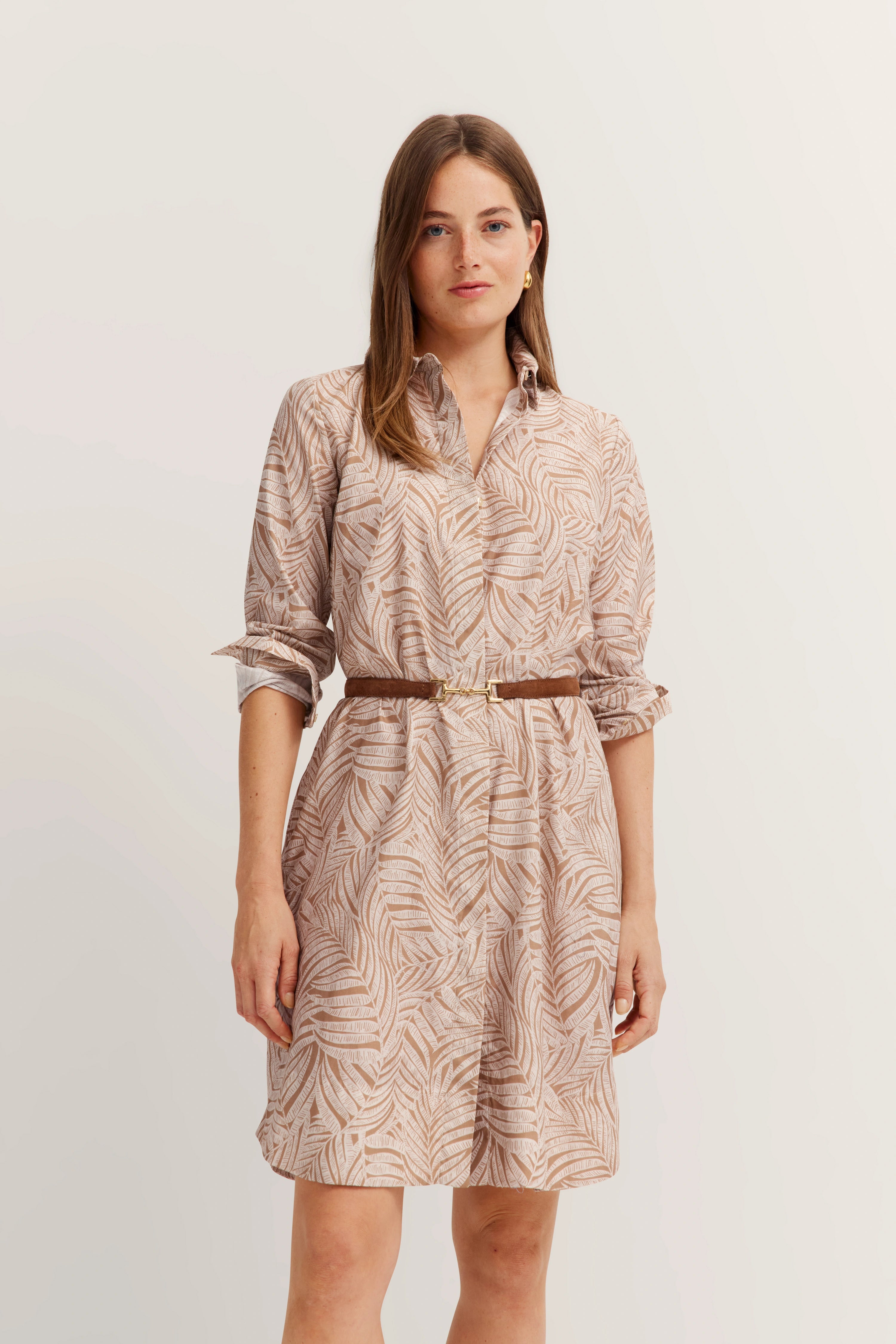 Model in beige patterned shirt dress with brown belt, relaxed pose.