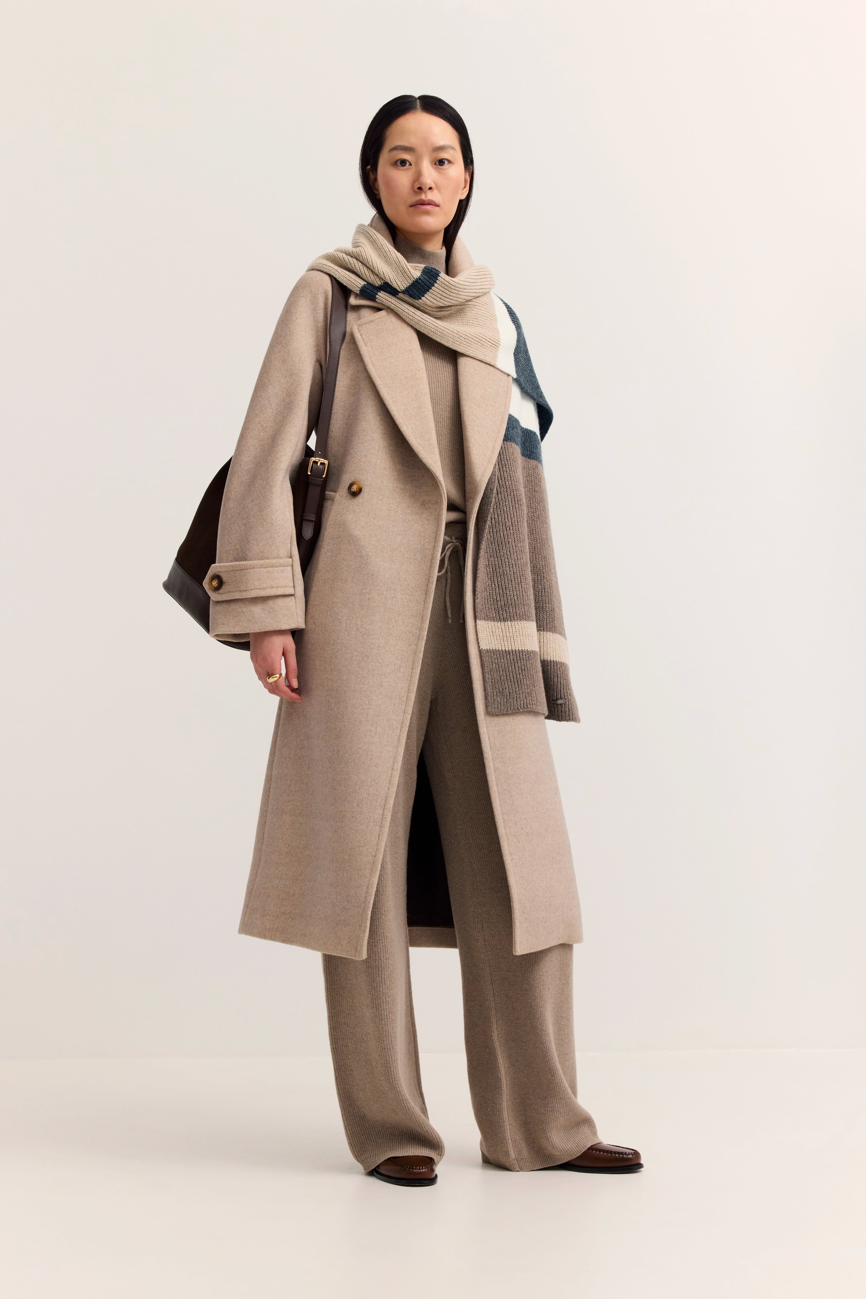 Beiges Outfit mit Mantel und Schal, Model posiert entspannt, bugatti Stil.