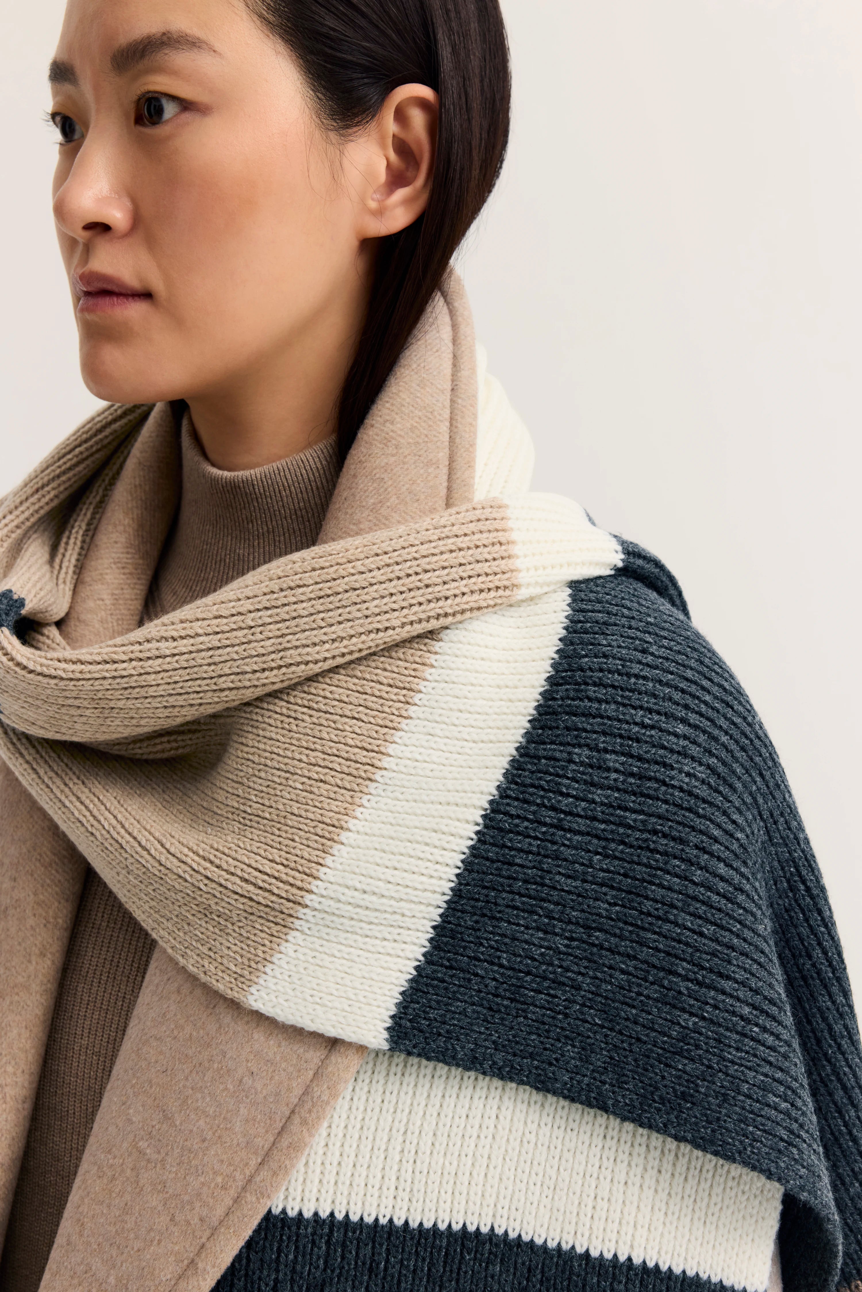 Modelbild im Profil, beige Rollkragenpullover mit beige-schwarz-weißem Strickschal von bugatti.