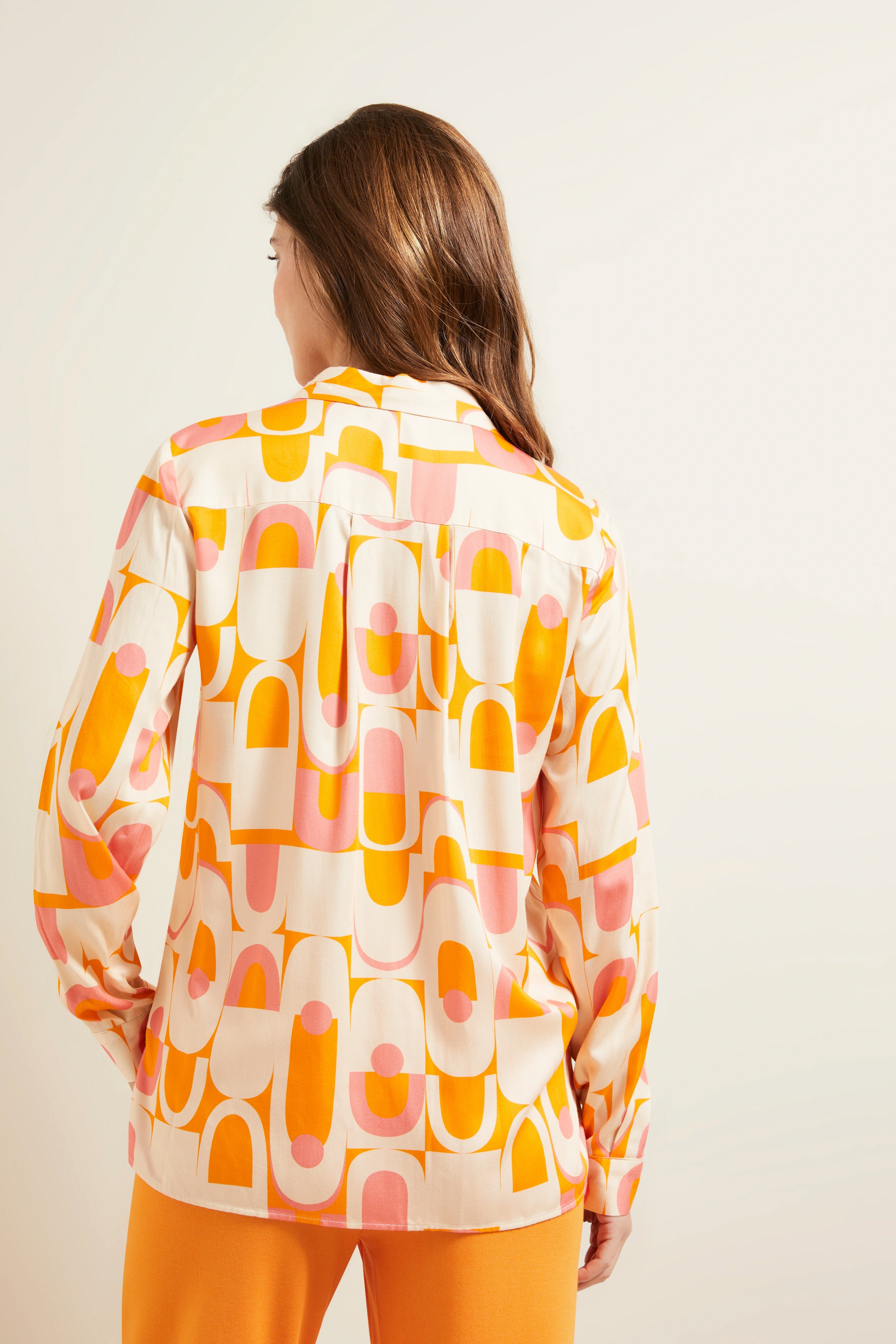 Bluse in Rosa-Orange-Muster, Rückansicht, Modell casual von hinten, kombiniert mit orangefarbener Hose.