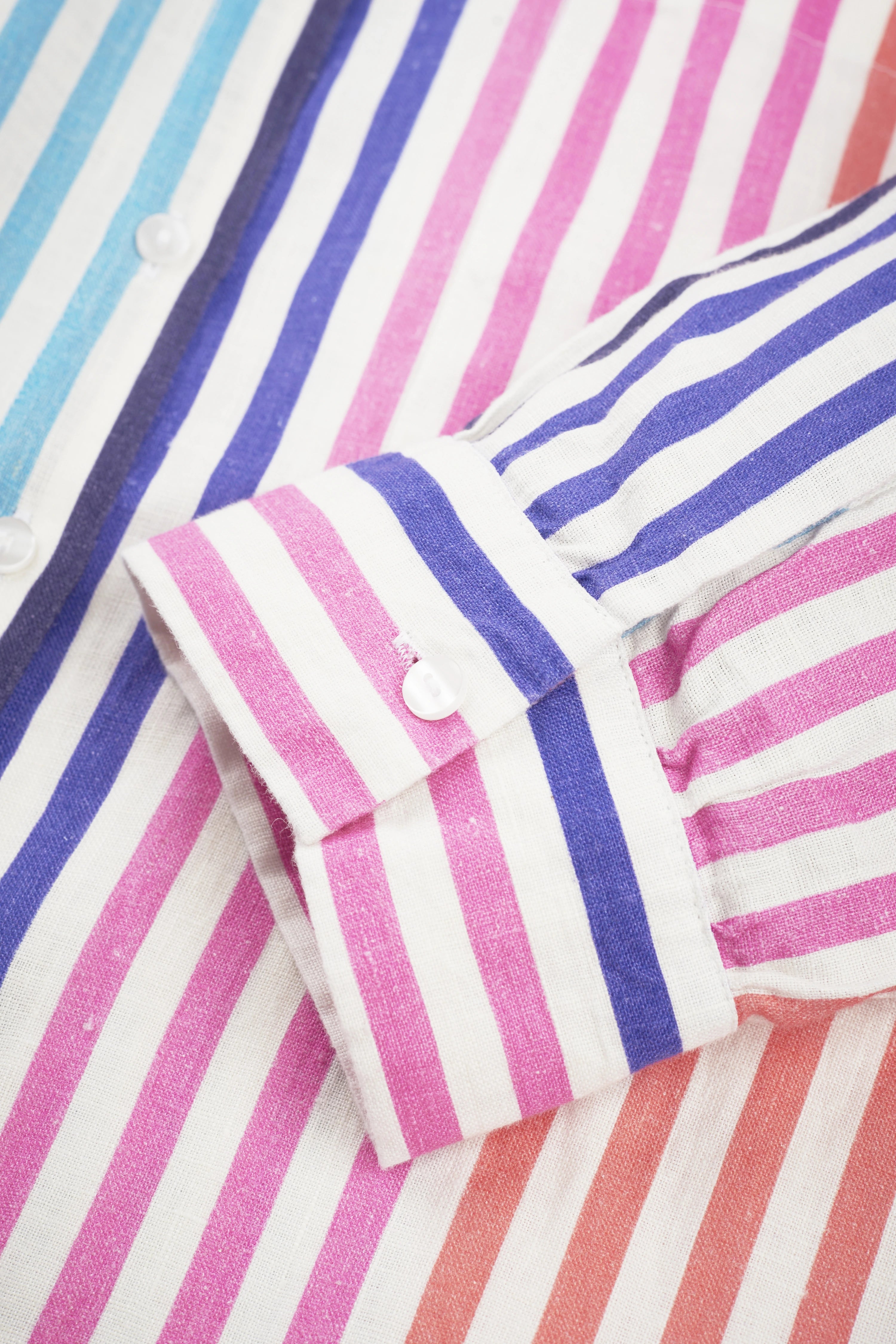 Striped shirt in pink, blue, and white, close-up. Hanger, button detail. No model.