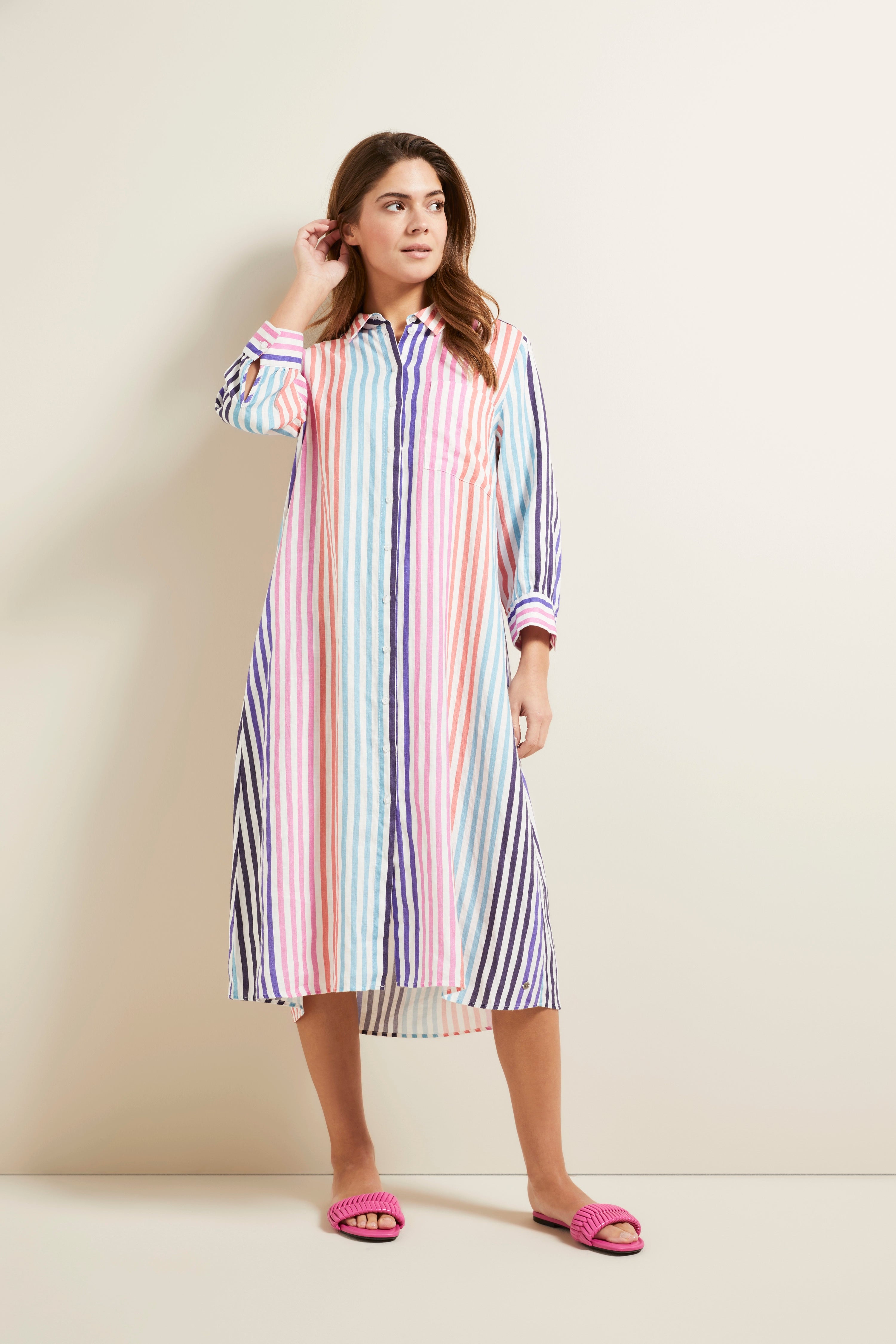 Model in striped bugatti shirt dress, pastel colors, standing, hand in hair, pink sandals.