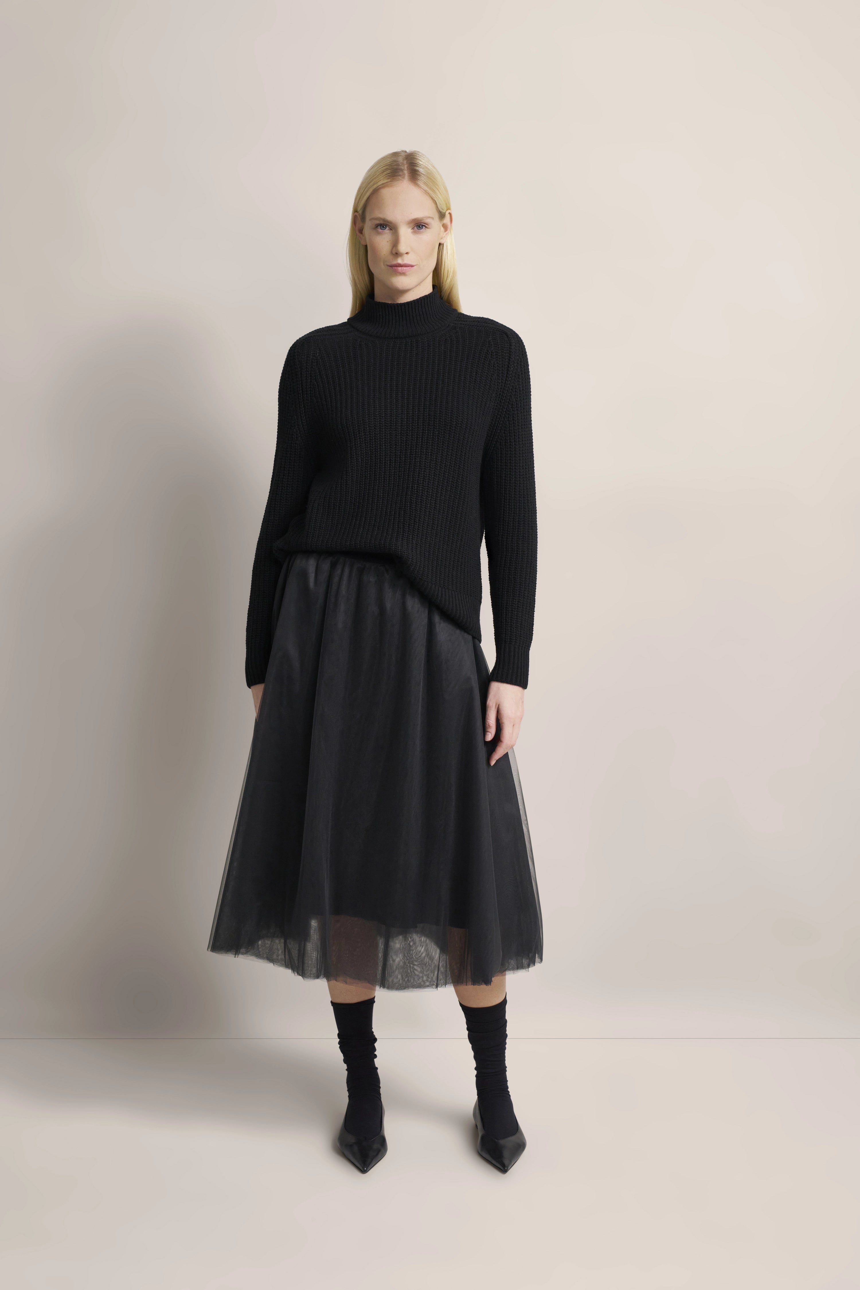 Schwarzer Pullover und Tüllrock, Modelbild, aufrecht stehend, ruhige Pose, bugatti Stil.