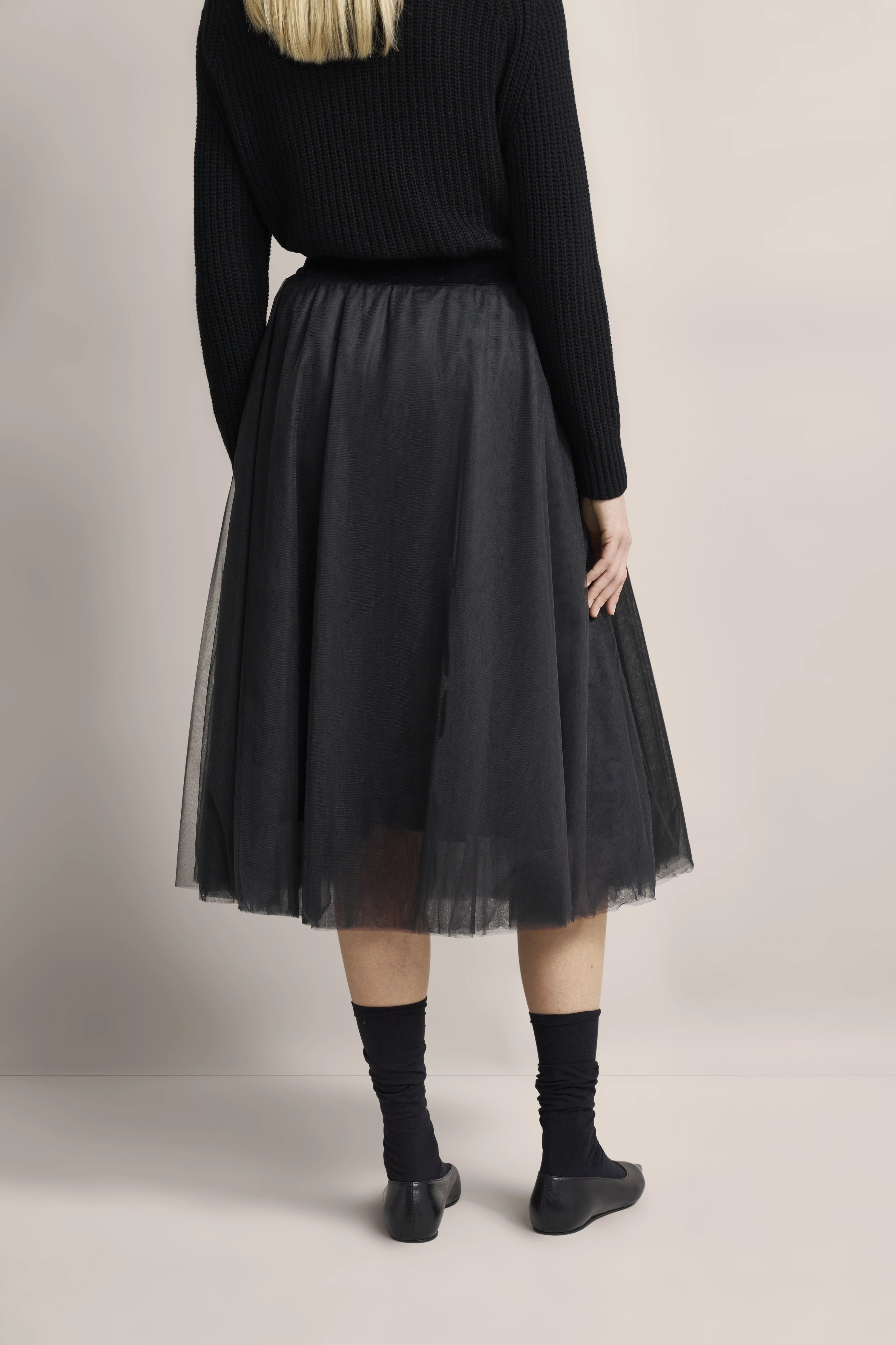 Schwarzer Pullover und Tüllrock in Modelaufnahme, Rückenansicht, entspanntes Posen.