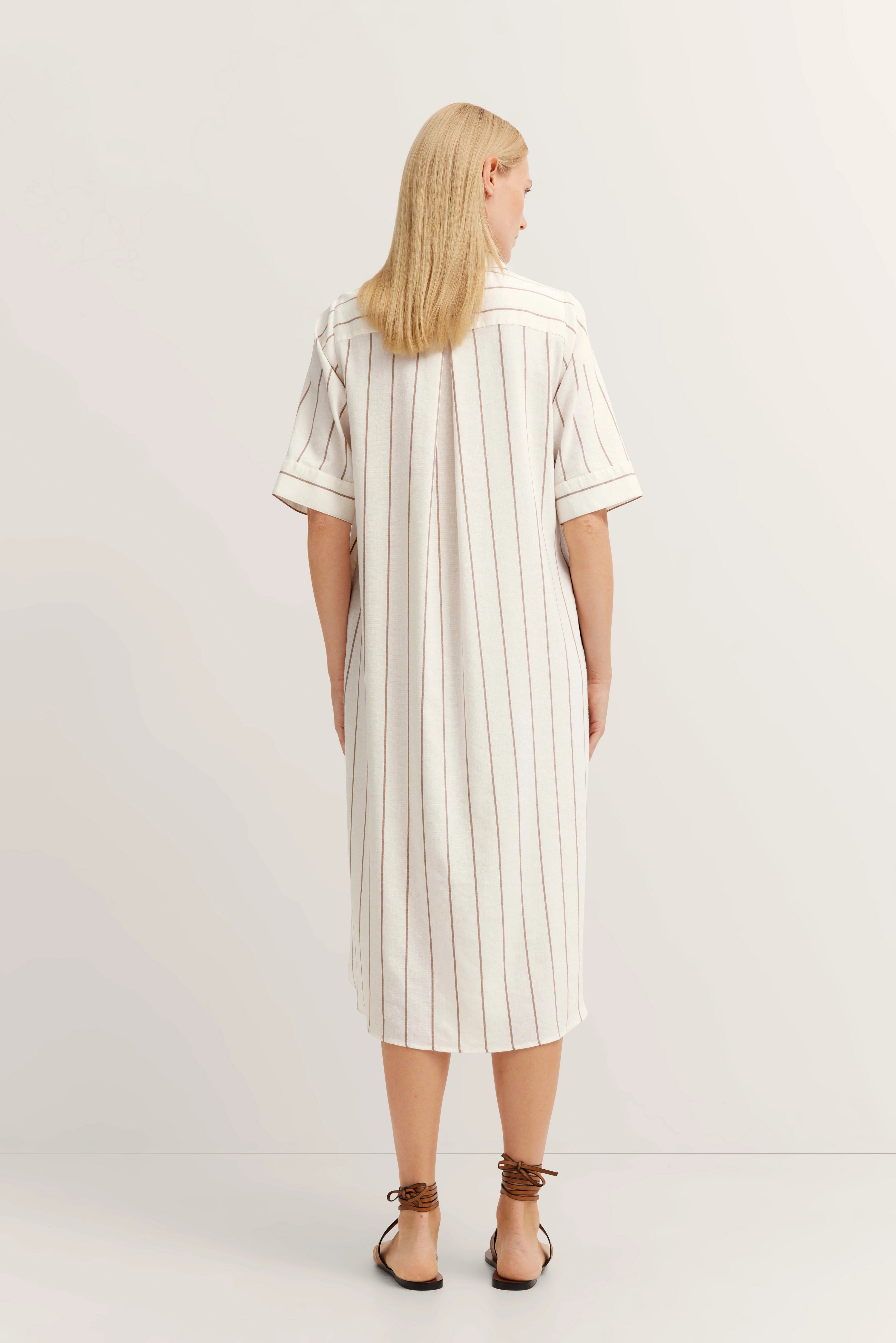 Back view: Model in white dress with brown stripes, casual pose.