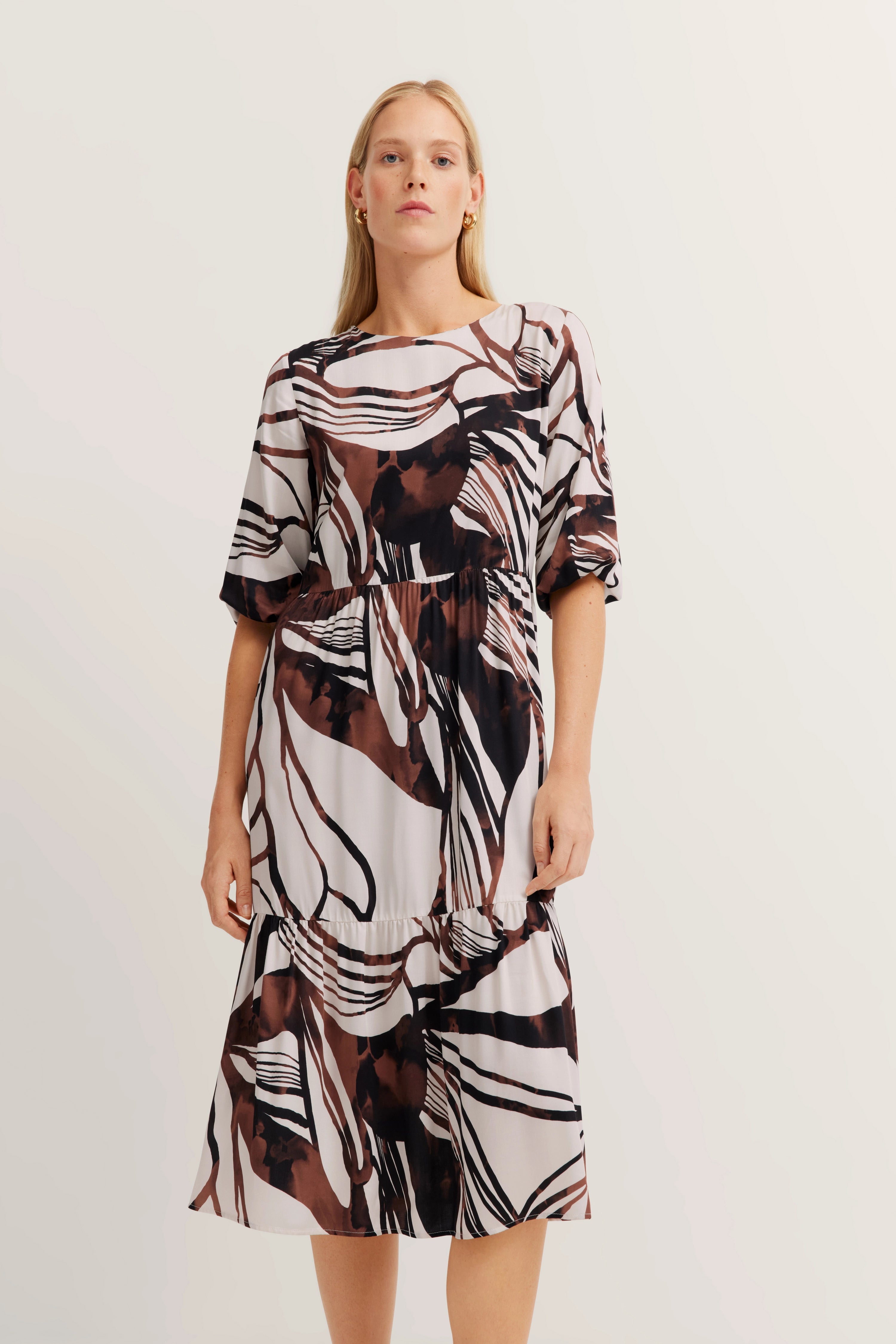 Model wears midi dress with abstract brown and white pattern, standing pose.