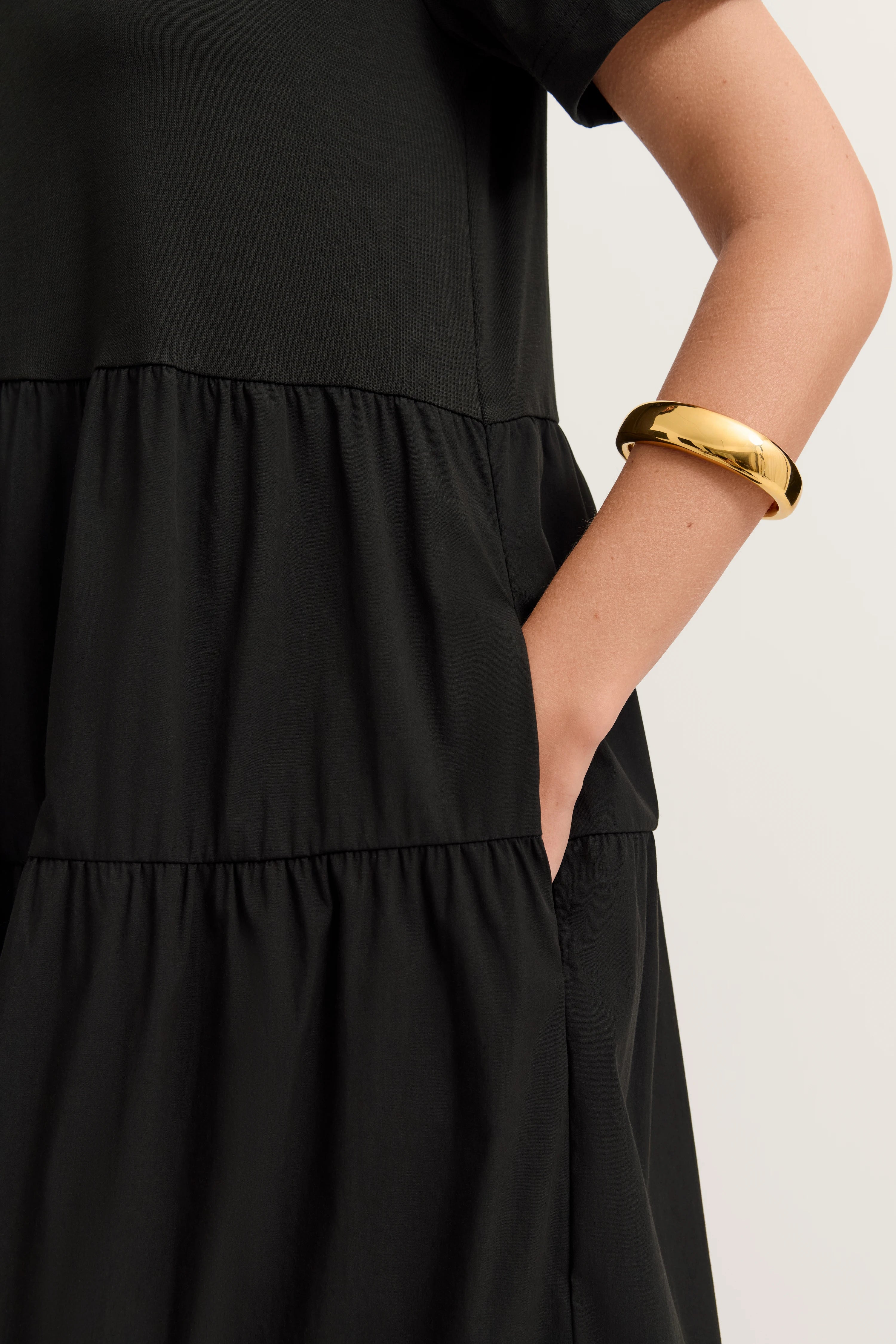 Schwarzes bugatti Kleid mit Stufen, legerer Stil, goldener Armreif, Detailansicht.