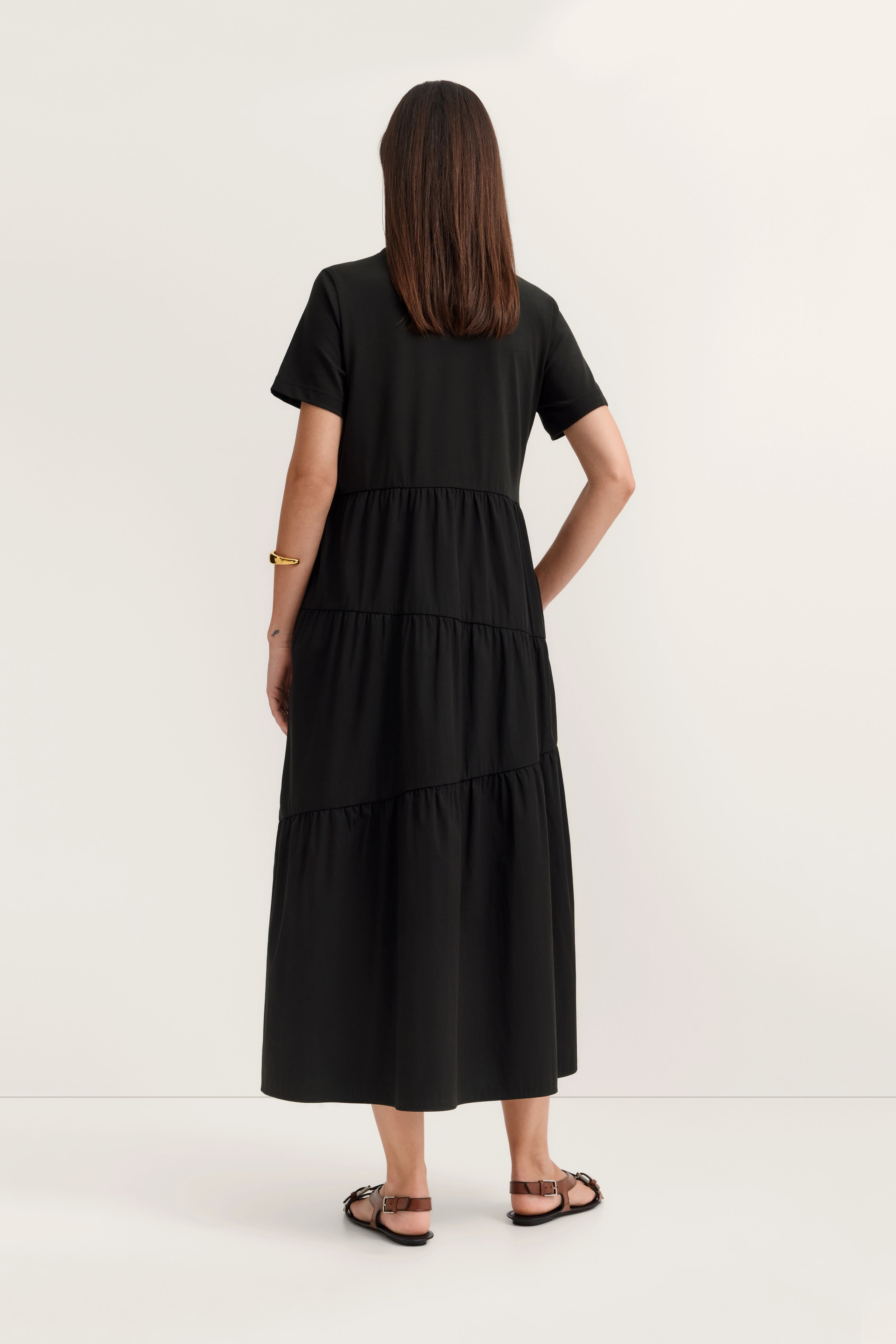 Schwarzes Stufenkleid, Rückenansicht, legeres Modelbild mit entspanntem Stand.