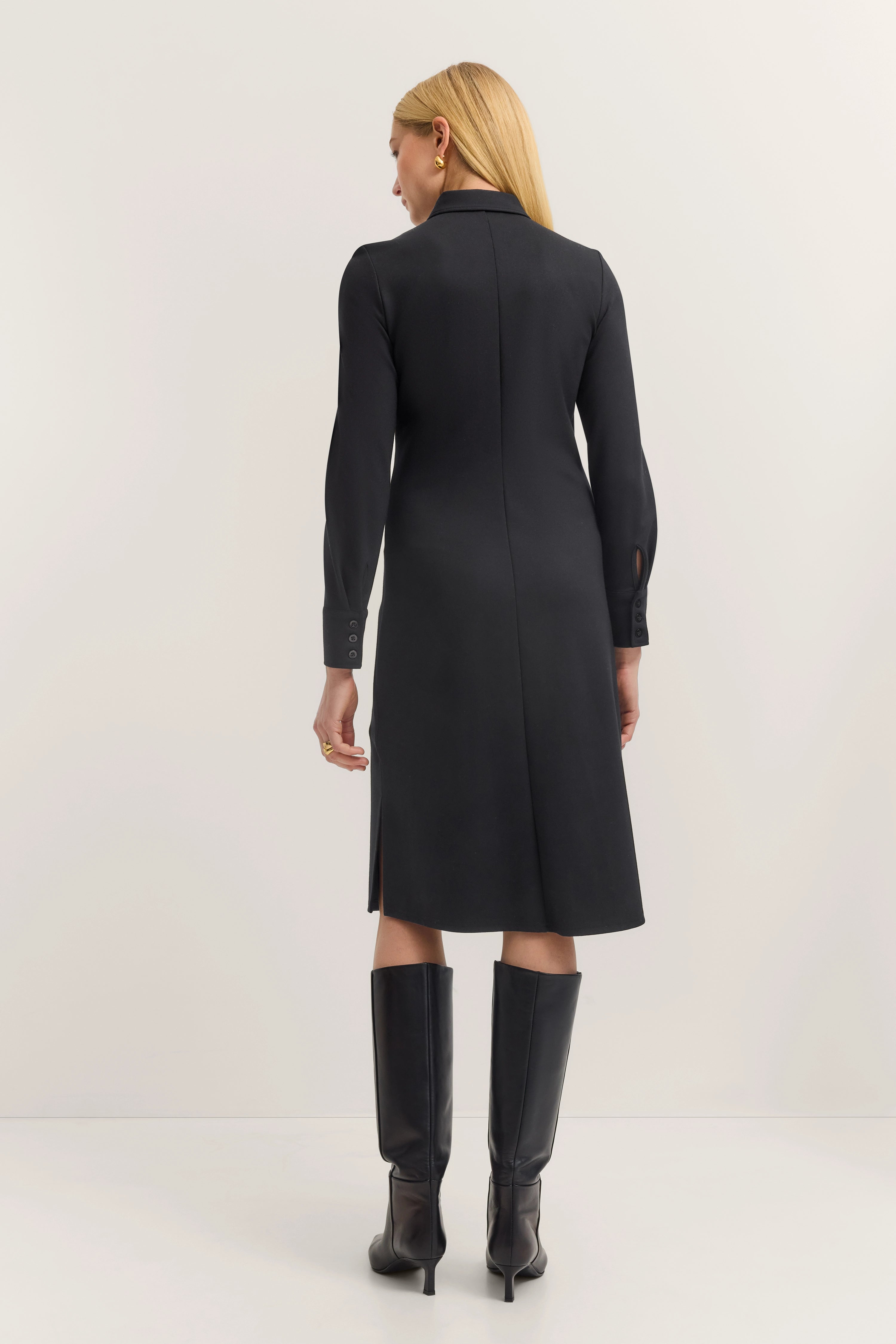 Schwarzes bugatti Kleid, Model von hinten, Stehpose, kombiniert mit hohen schwarzen Stiefeln.