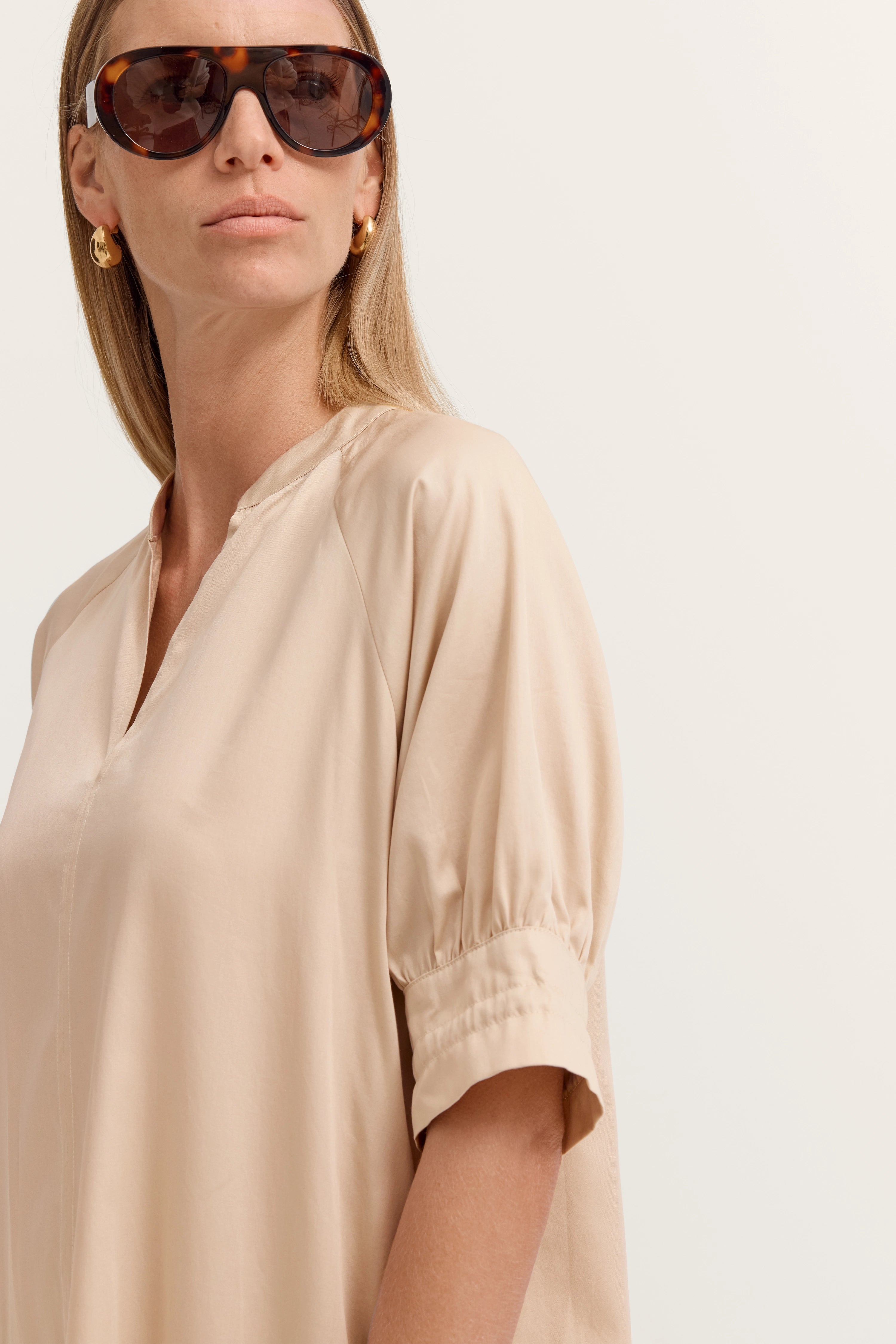 Beiges bugatti Kleid, Büstenbild, lässige Eleganz, goldene Ohrringe, große Sonnenbrille.