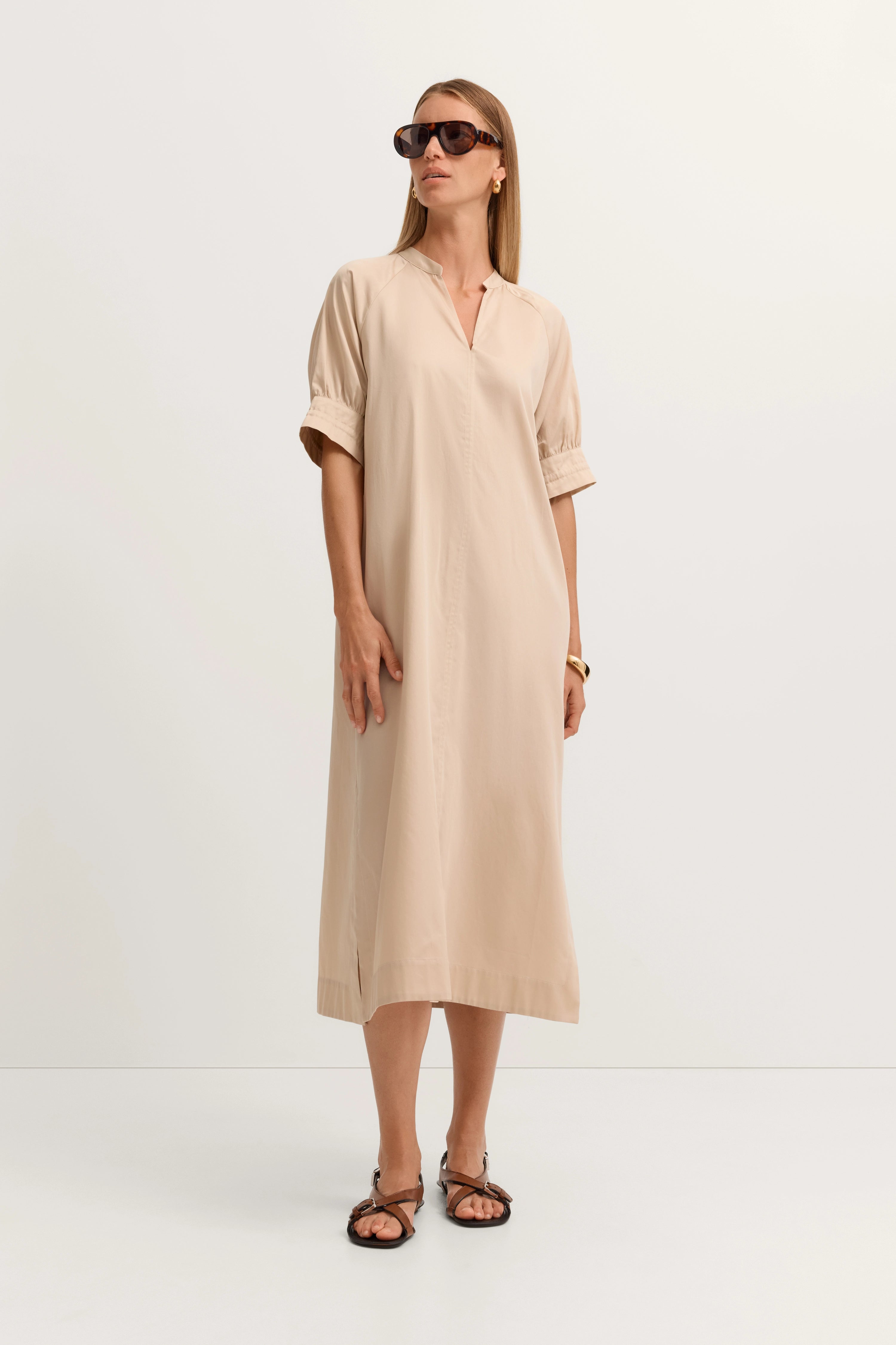 Beiges bugatti Kleid, Modellbild, lässig stehend, mit Sonnenbrille und Sandalen.