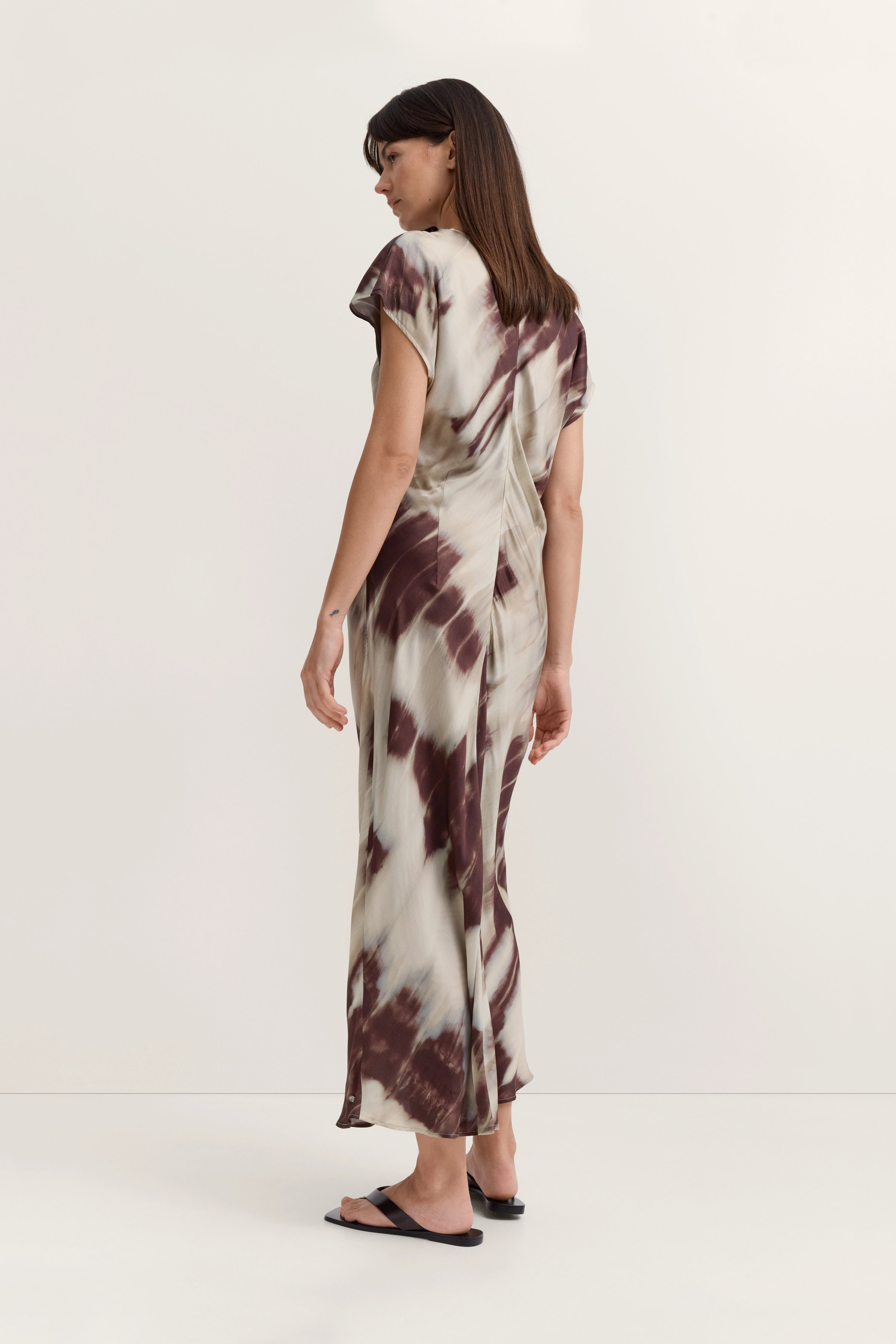 Langes Kleid mit abstraktem Muster in Beige und Braun, Model im Profil, entspanntes Posing.