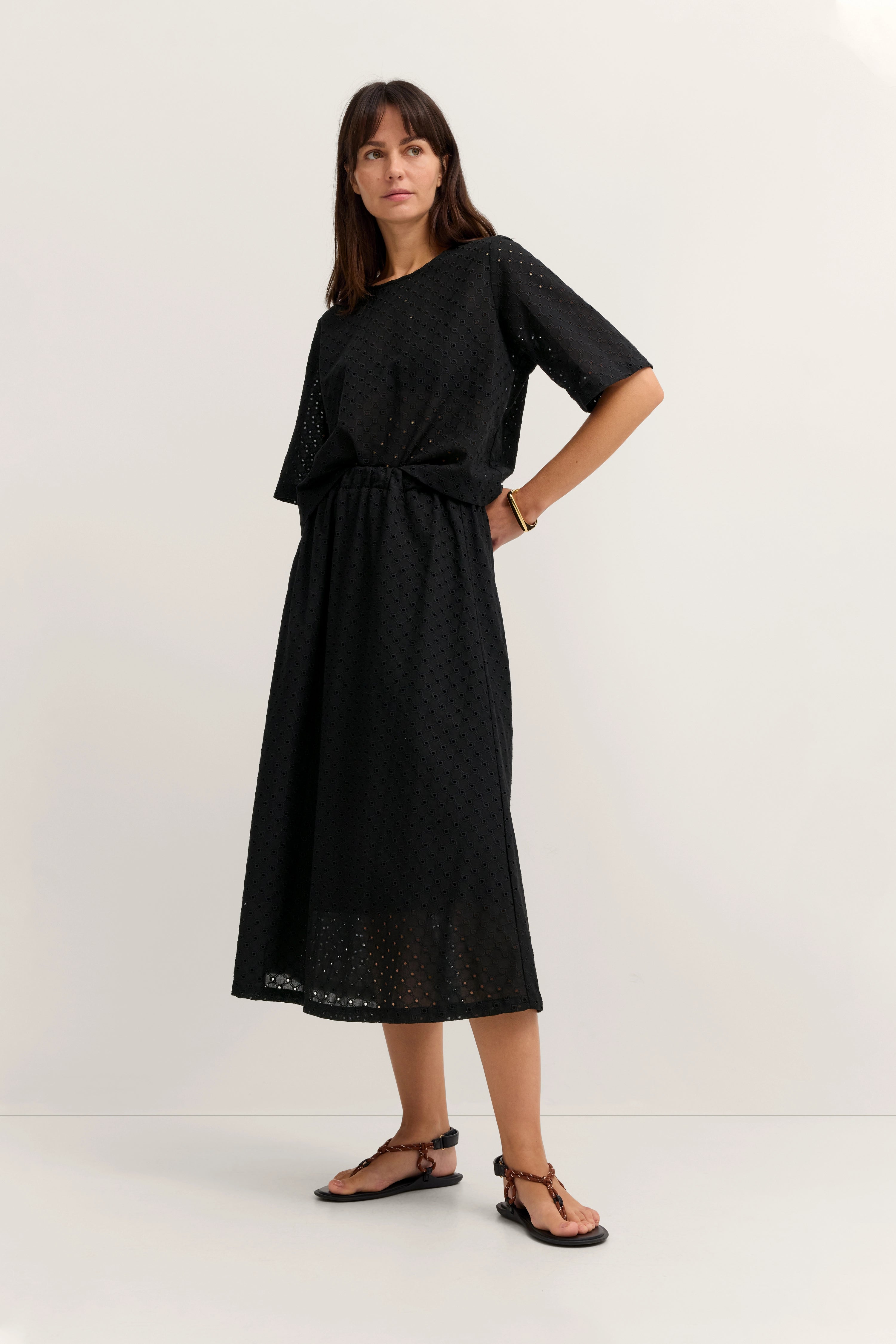 Model trägt schwarzes Lochmuster-Kleid von bugatti, stehend, Hände in der Taille.