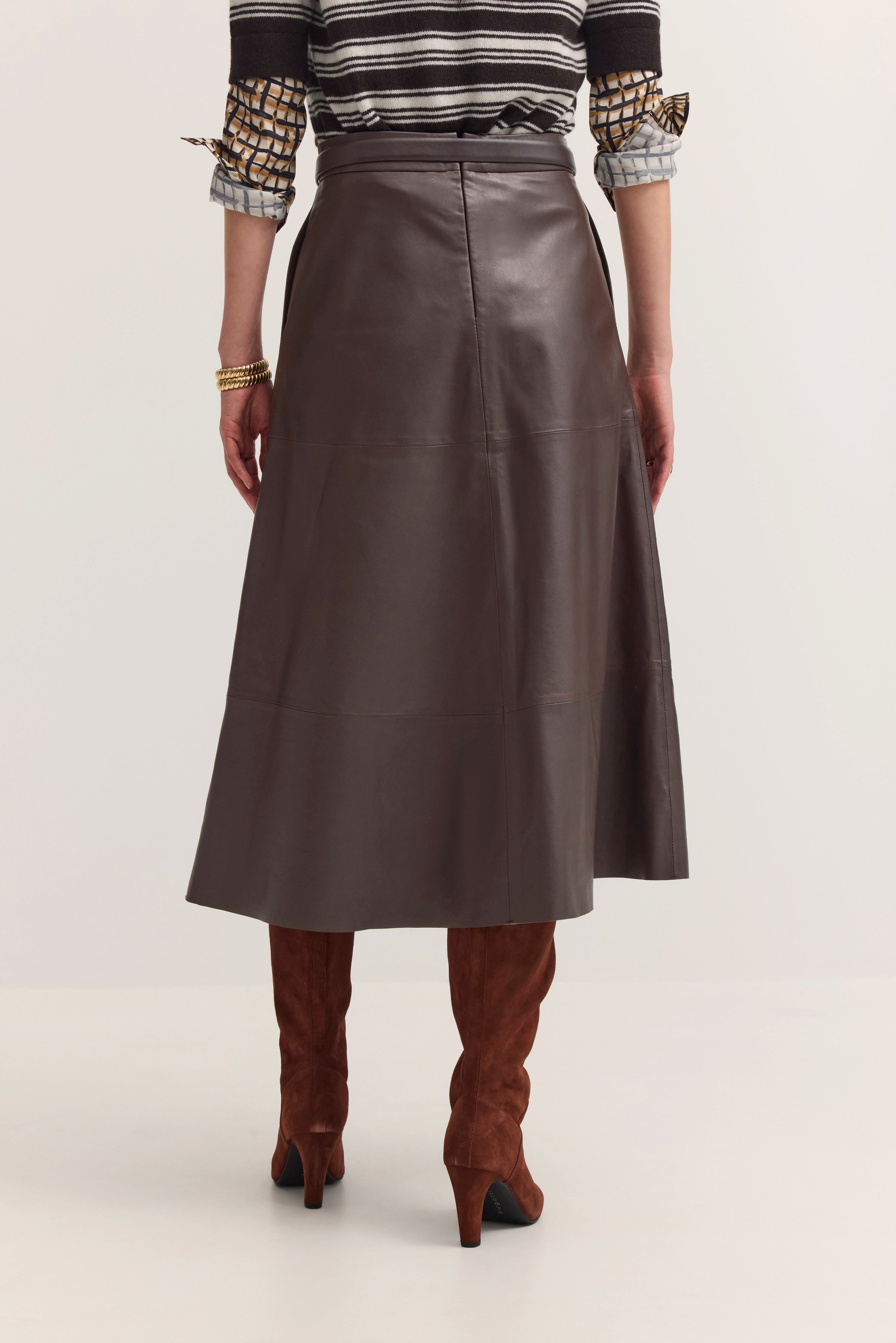 Brauner Lederrock, gestreifter Pullover, Model von hinten, braune Stiefel, elegantes Outfit von bugatti.