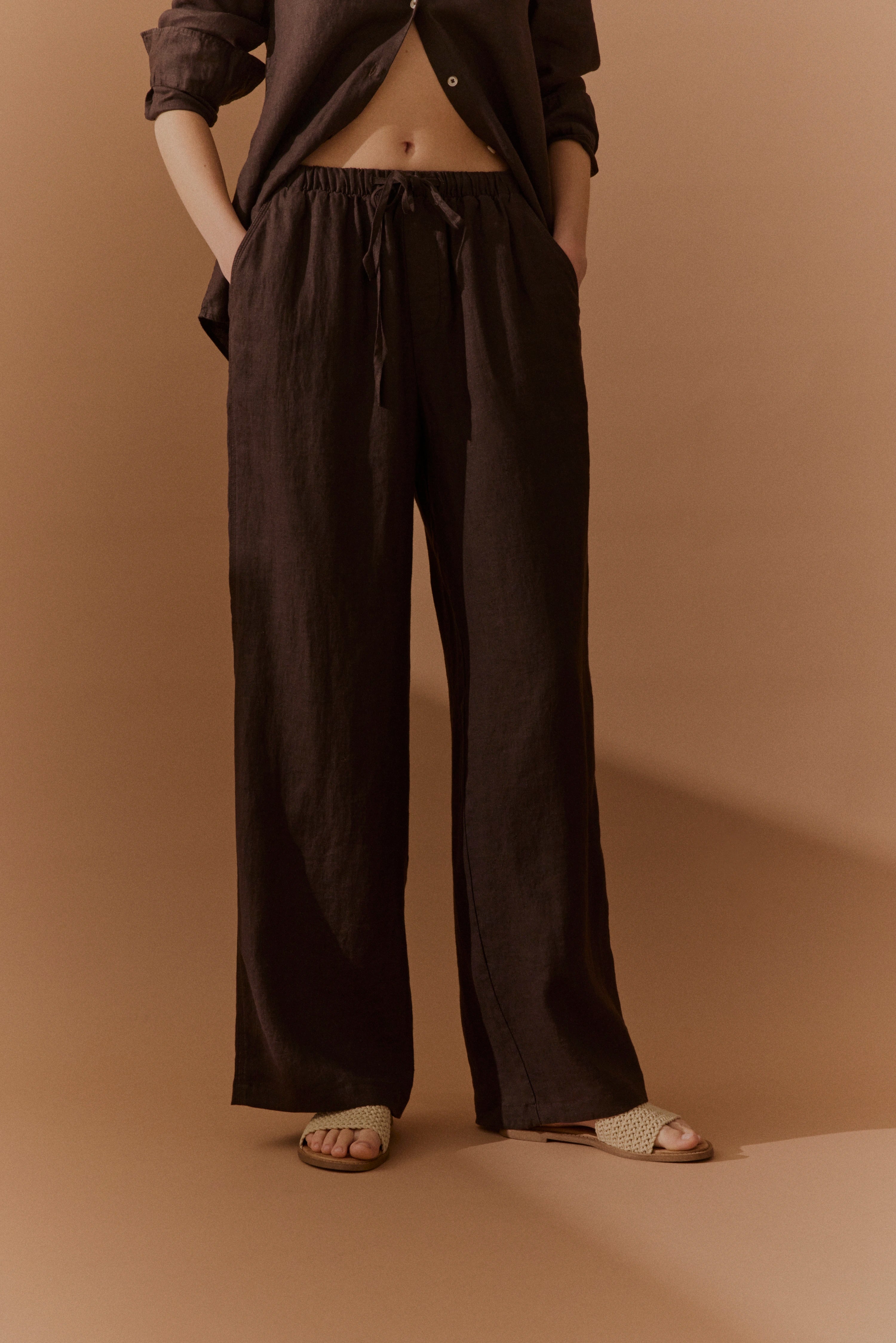 Braunes Leinen-Outfit, locker geschnittene Hose und Hemd, legeres Modelbild, entspannte Pose.