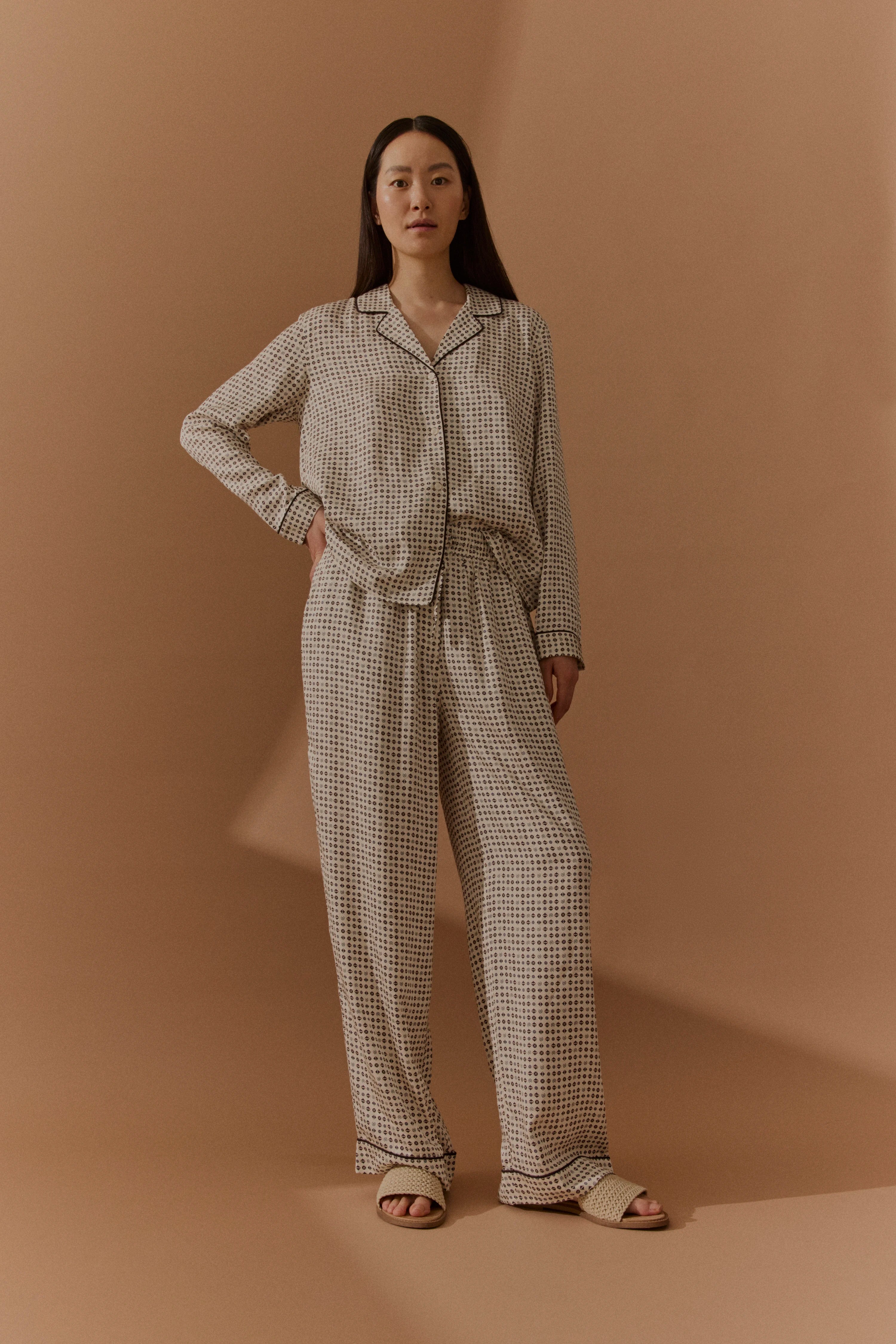 Model in gemusterter Pyjama-Set in Beige und Schwarz, entspannte Pose.