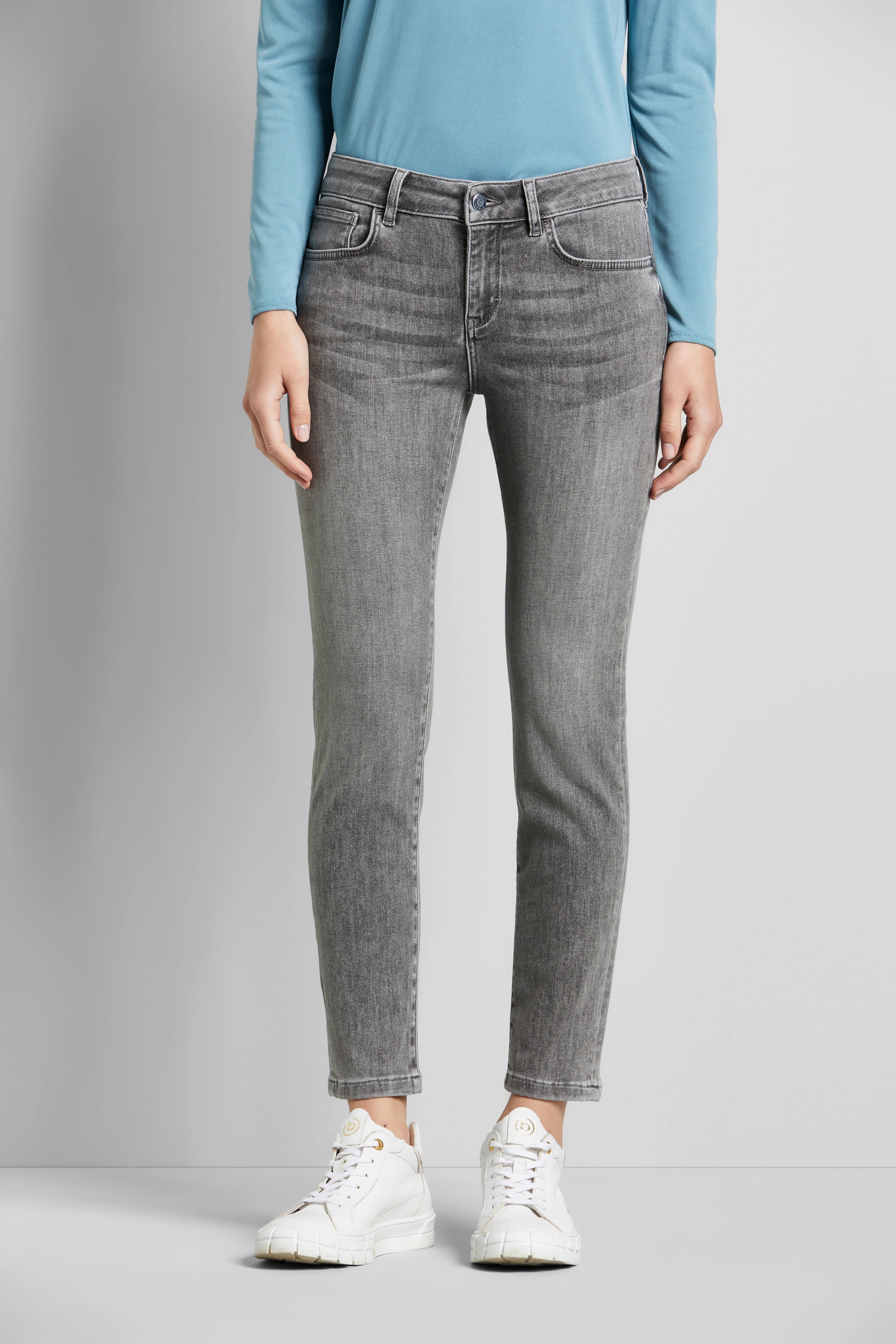 Graues Jeans-Outfit mit blauem Oberteil, weiße Sneaker. Büstenbild, lässiger Look. bugatti Stil.