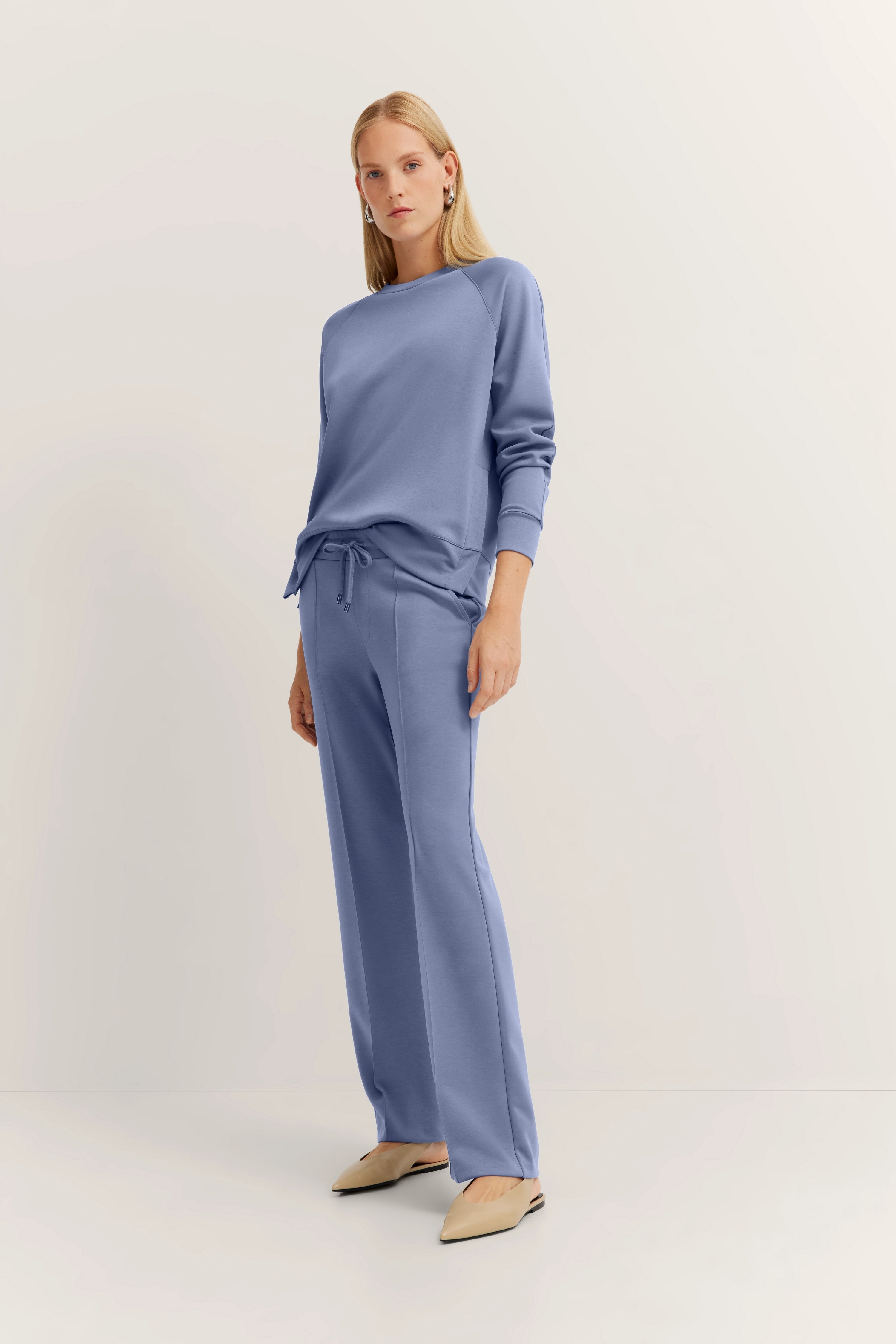 Model in casual, lichtblauw bugatti-outfit met sweatshirt en joggingbroek, staat ontspannen.