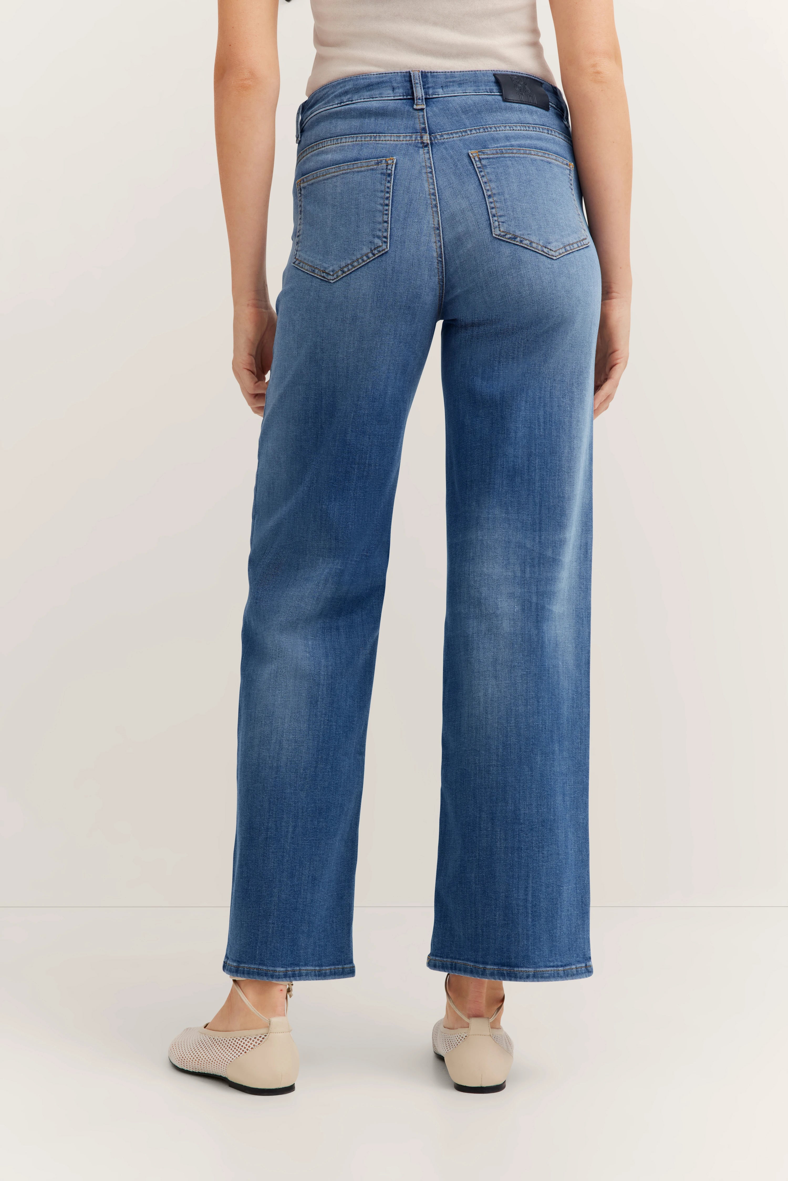 Jeans in blauw, casual fit, gedragen door model achterwaarts, gecombineerd met beige schoenen.