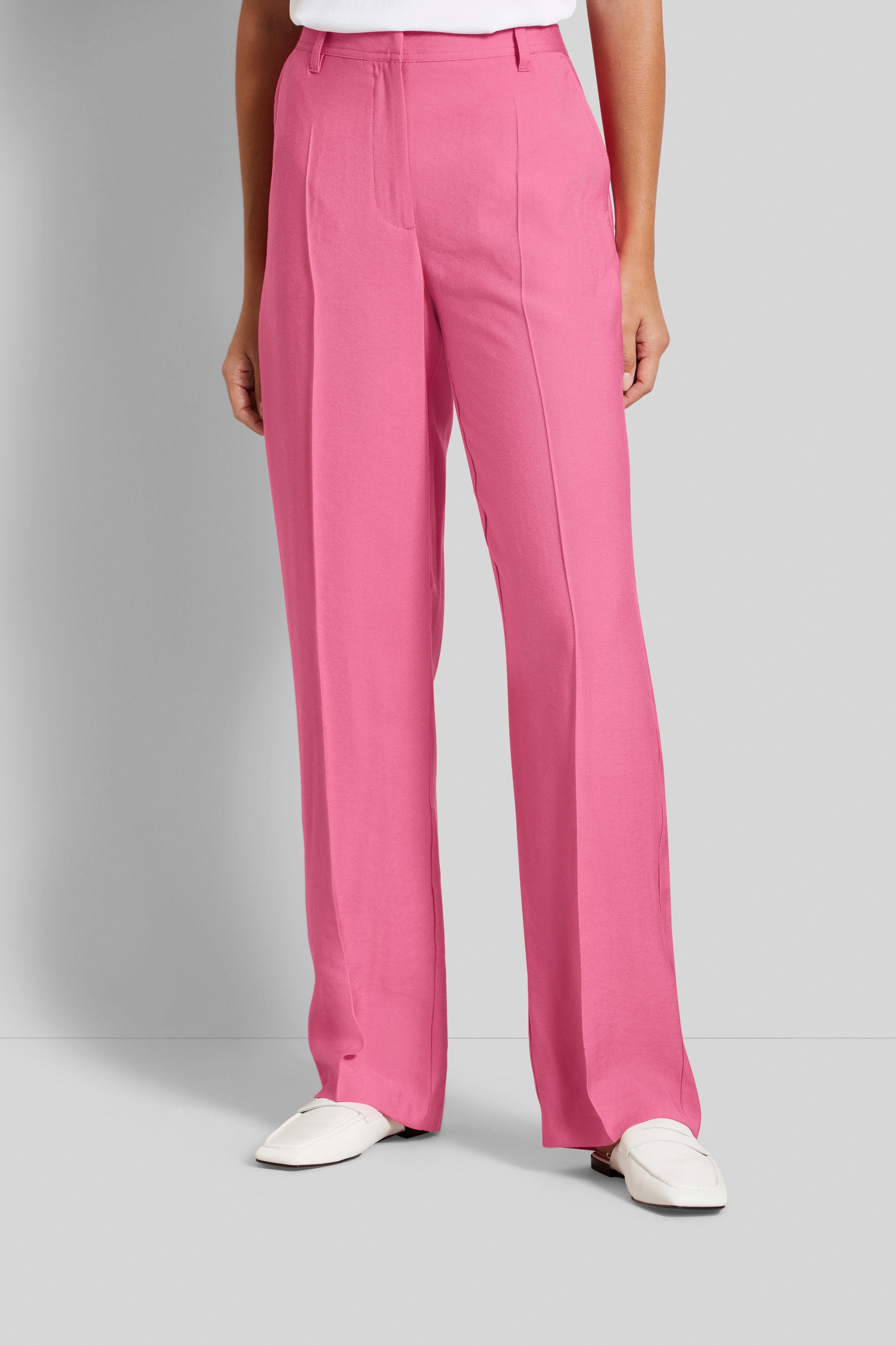 Roze bugatti broek, casual modelpose, nonchalant met witte schoen.