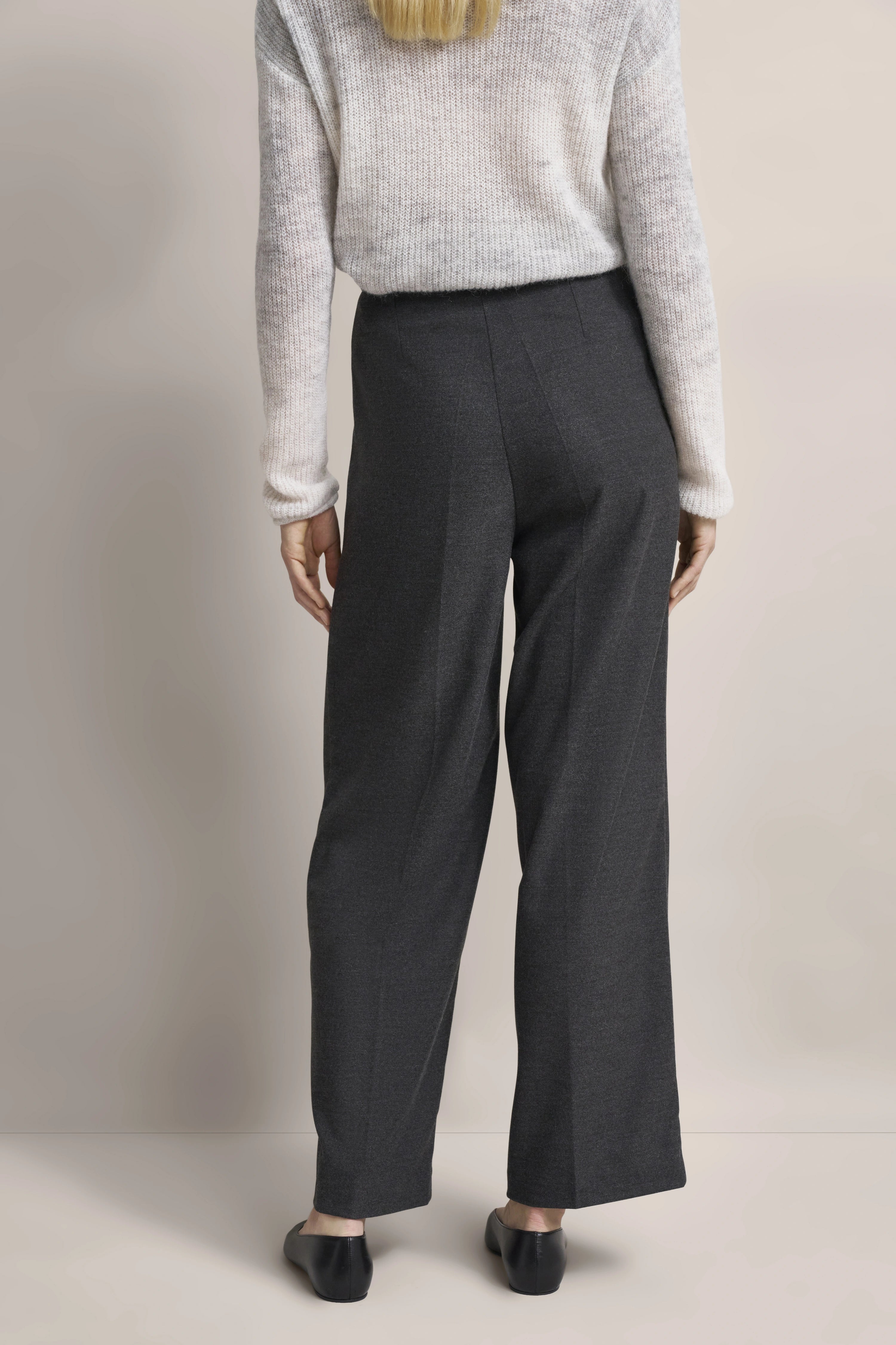 Grauer Wollpullover und dunkelgraue Hose, Modelbild von hinten, entspannte Pose.