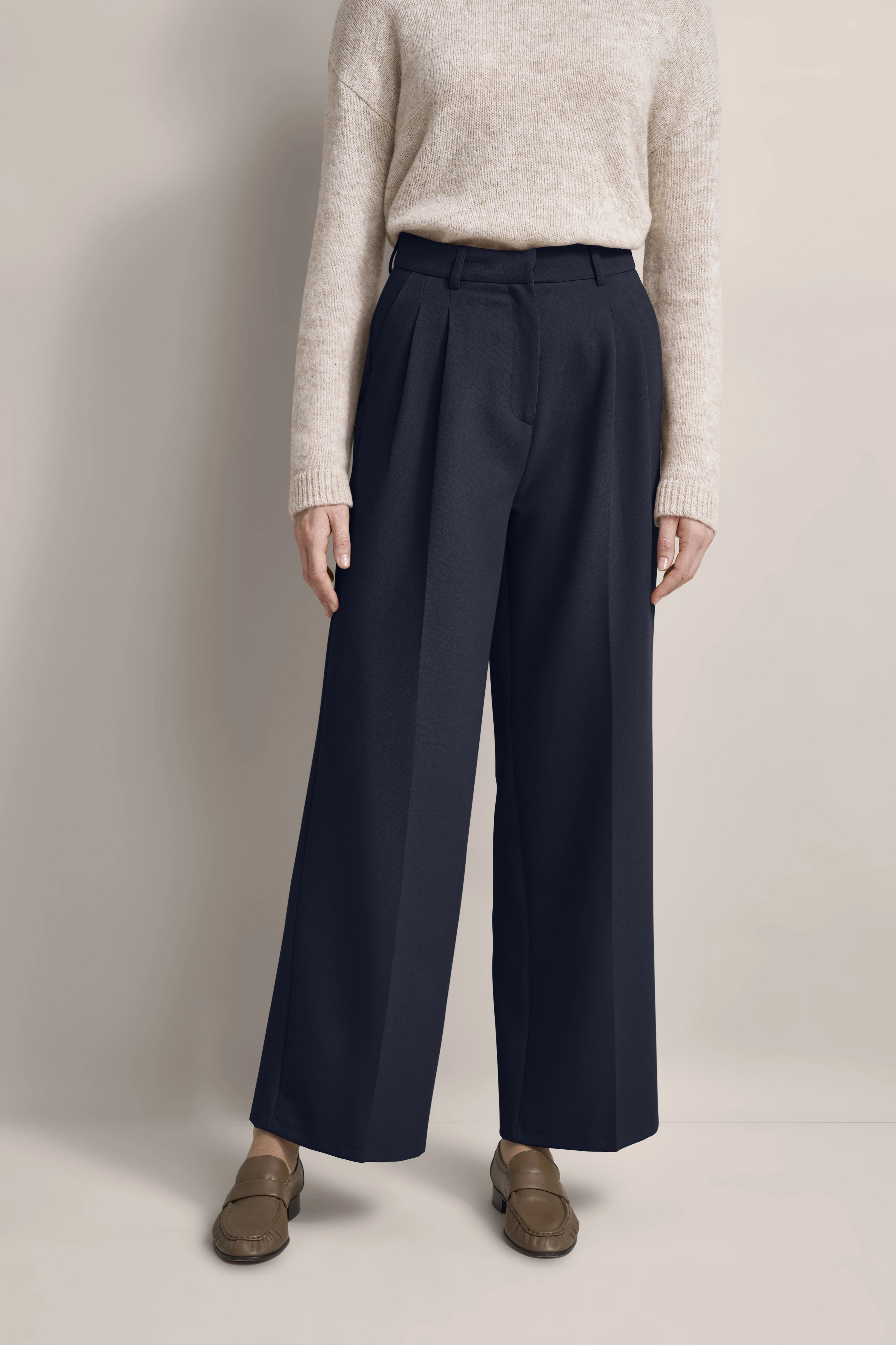 Beiger Pullover, marineblaue weite Hose, braune Loafer. Modelbild, legeres, entspanntes Posing.