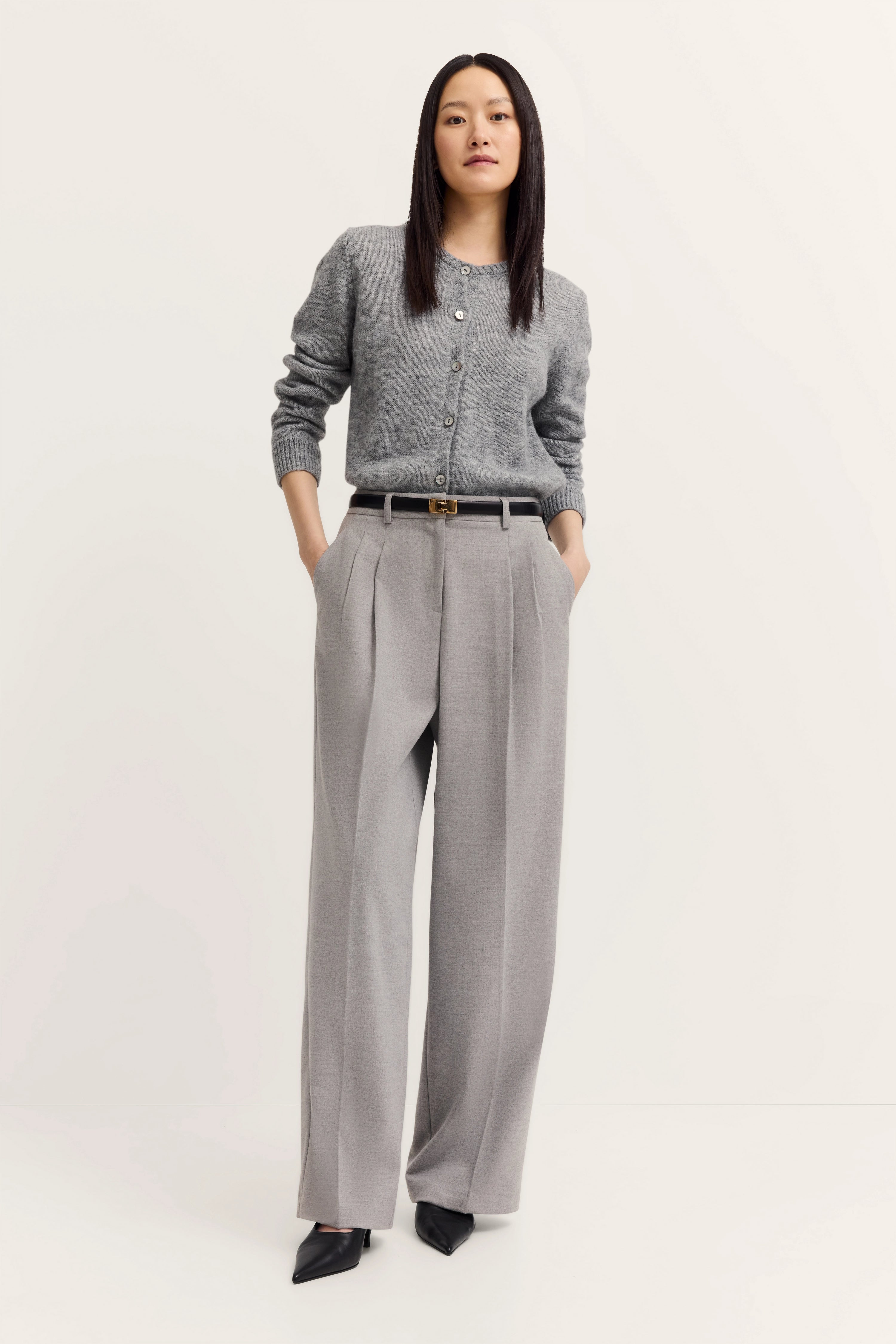 Grauer Cardigan und graue Hose, Model mit Händen in den Taschen, entspanntes Posing.
