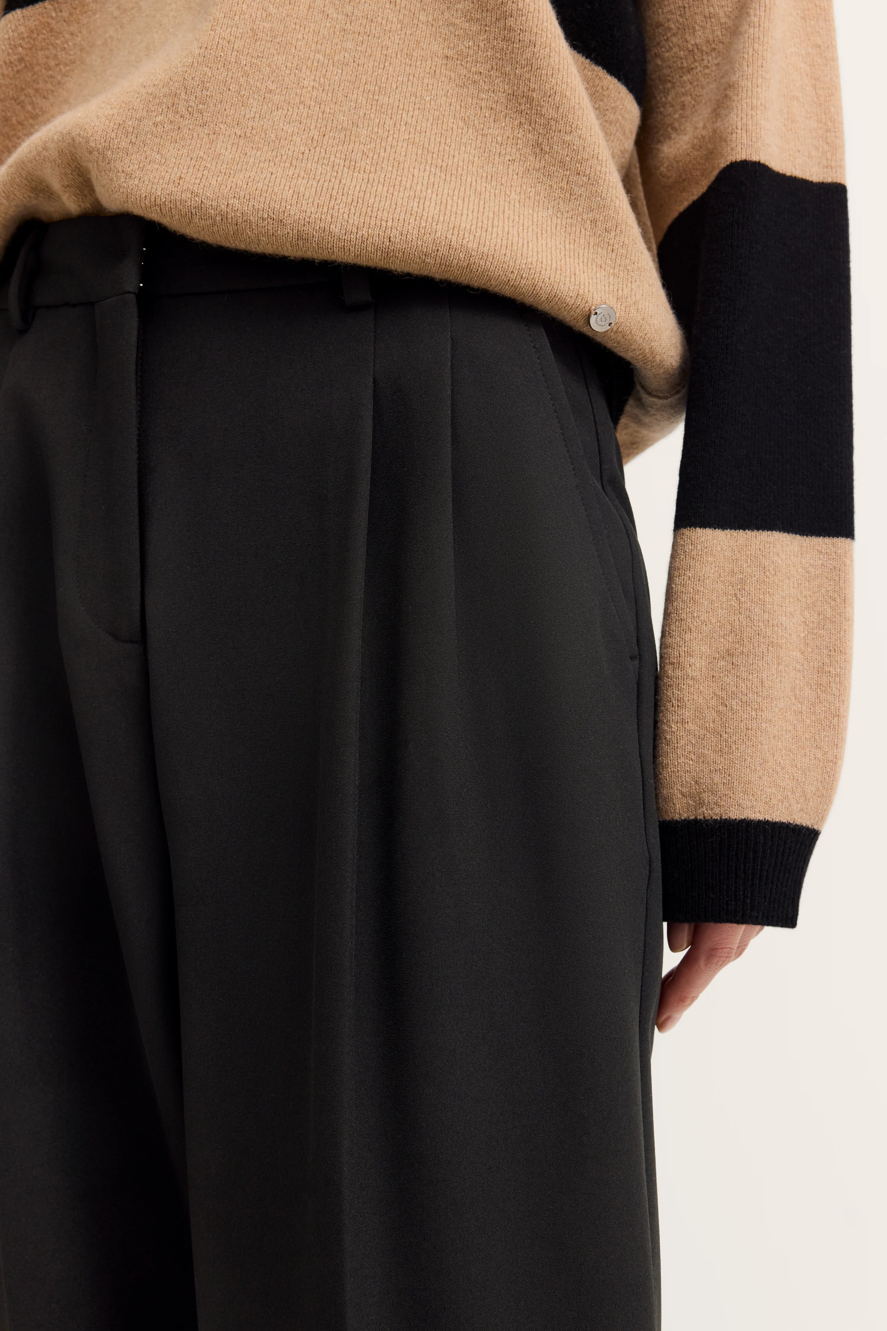 Beiger Pullover mit schwarzen Streifen, kombiniert mit schlichten schwarzen Hosen, legeres Büstenbild.