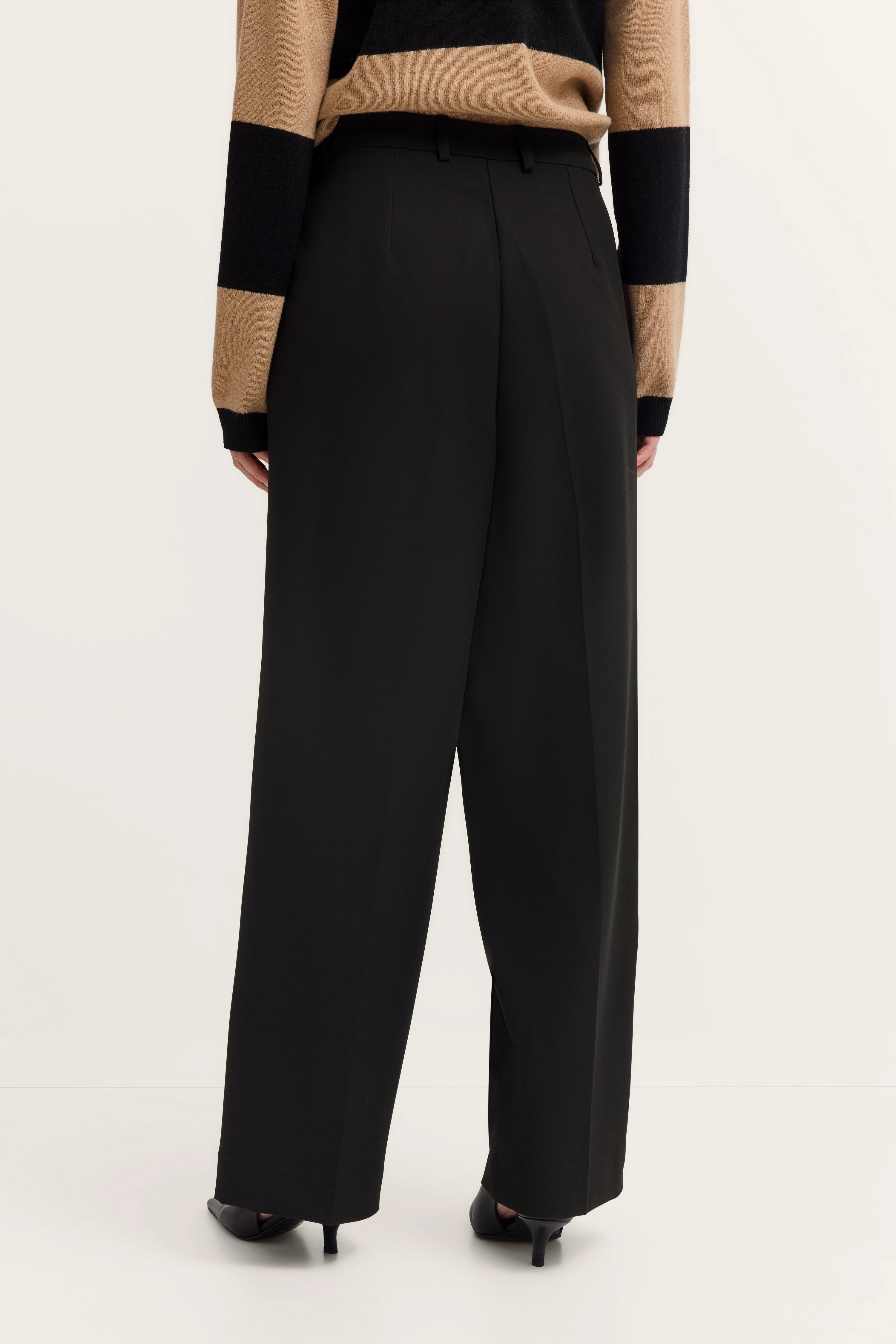 Schwarze Hose mit weitem Schnitt, gestreifter Pullover in Beige-Schwarz, Modelrückansicht.
