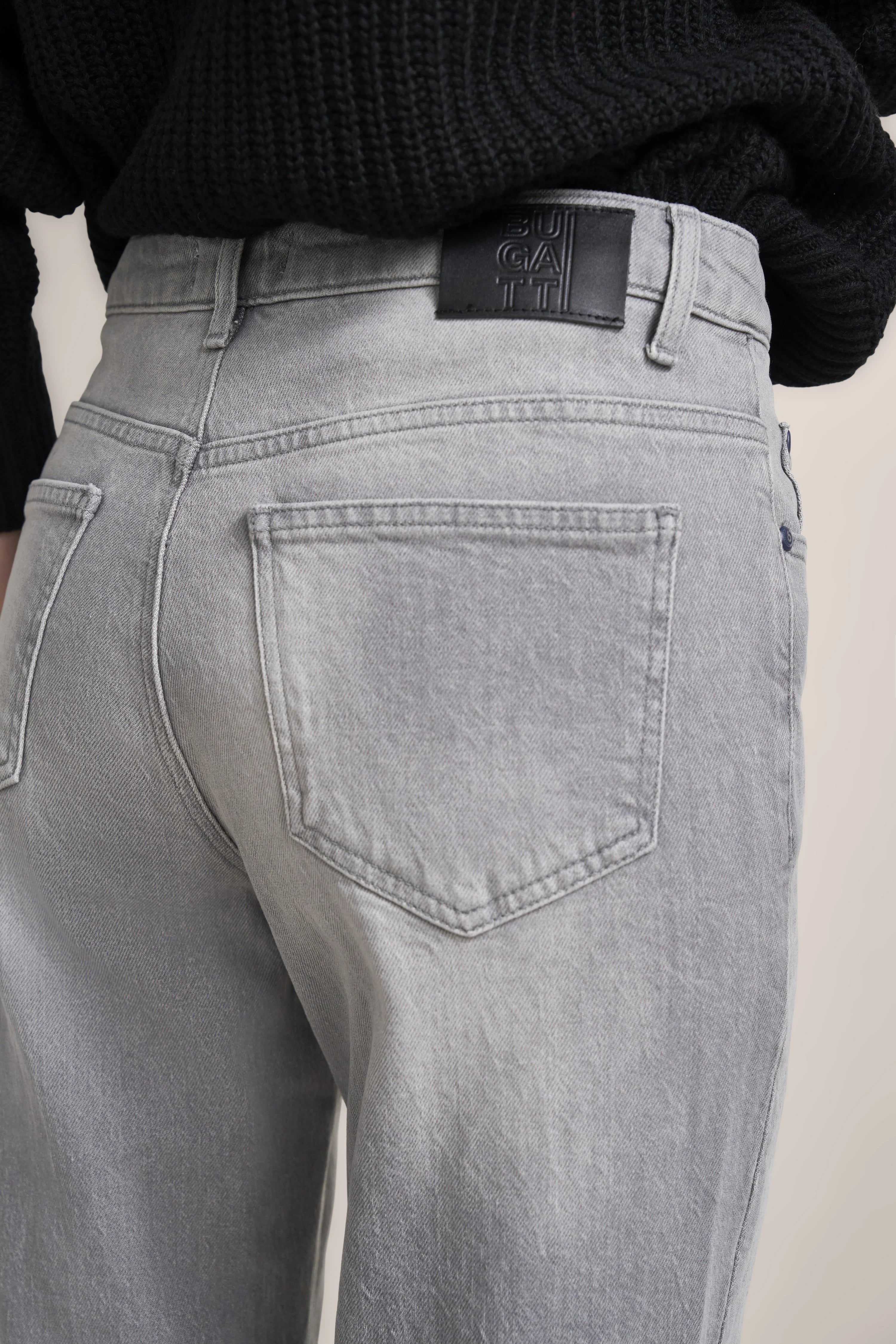 Graue bugatti Jeans, legeres Büstenbild, Detailansicht Gesäßtasche, kombiniert mit schwarzem Pullover.