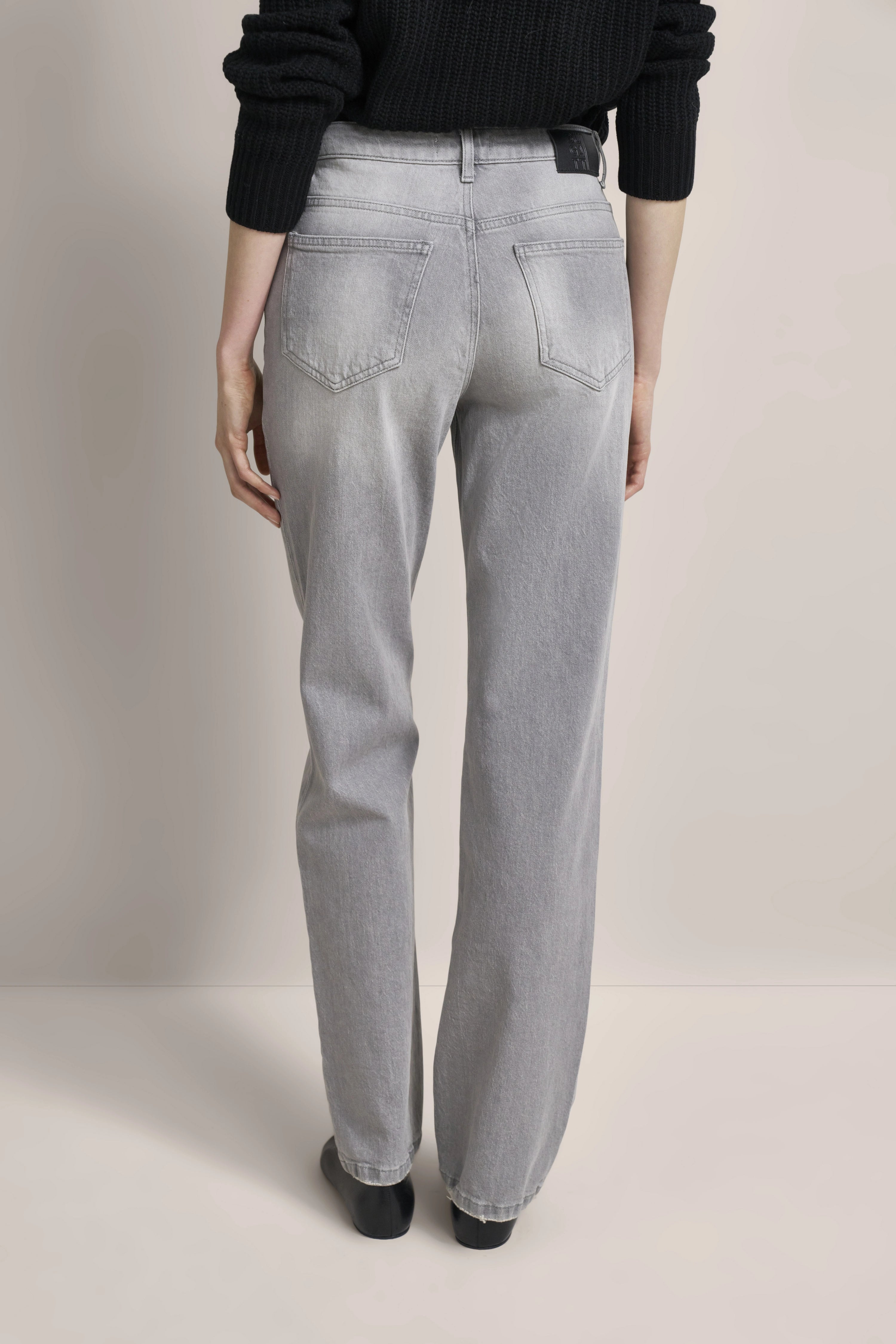 Graue Jeans, legeres Modelbild von hinten, schwarzer Pullover, entspannte Pose, zeitloser Stil von bugatti.