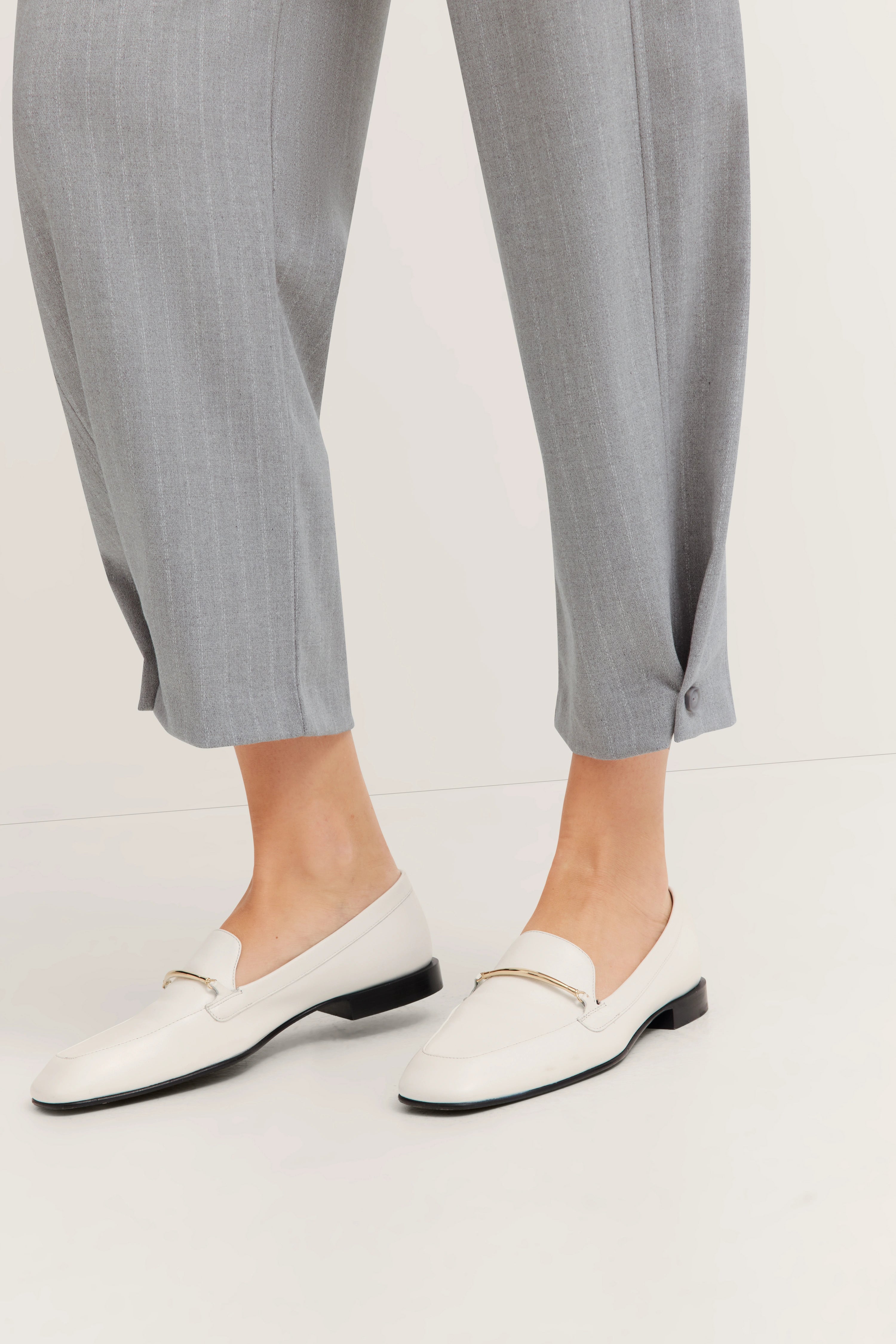Grijze broek met persvouwen, witte loafers van bugatti, stralen Italiaanse elegantie en kwaliteit uit.