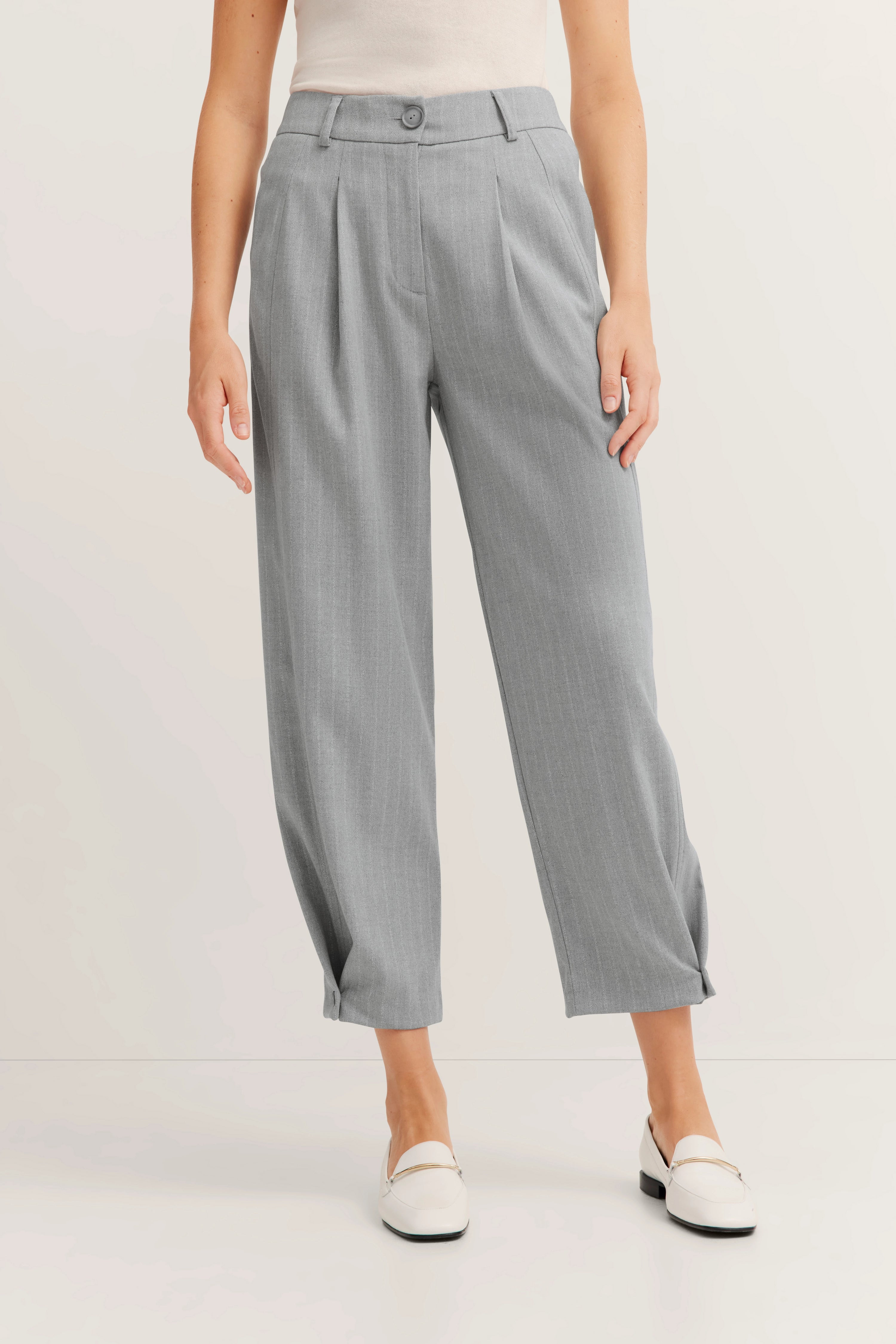 Grijze pantalon, ruim gesneden, buste, wit topje, witte loafers.