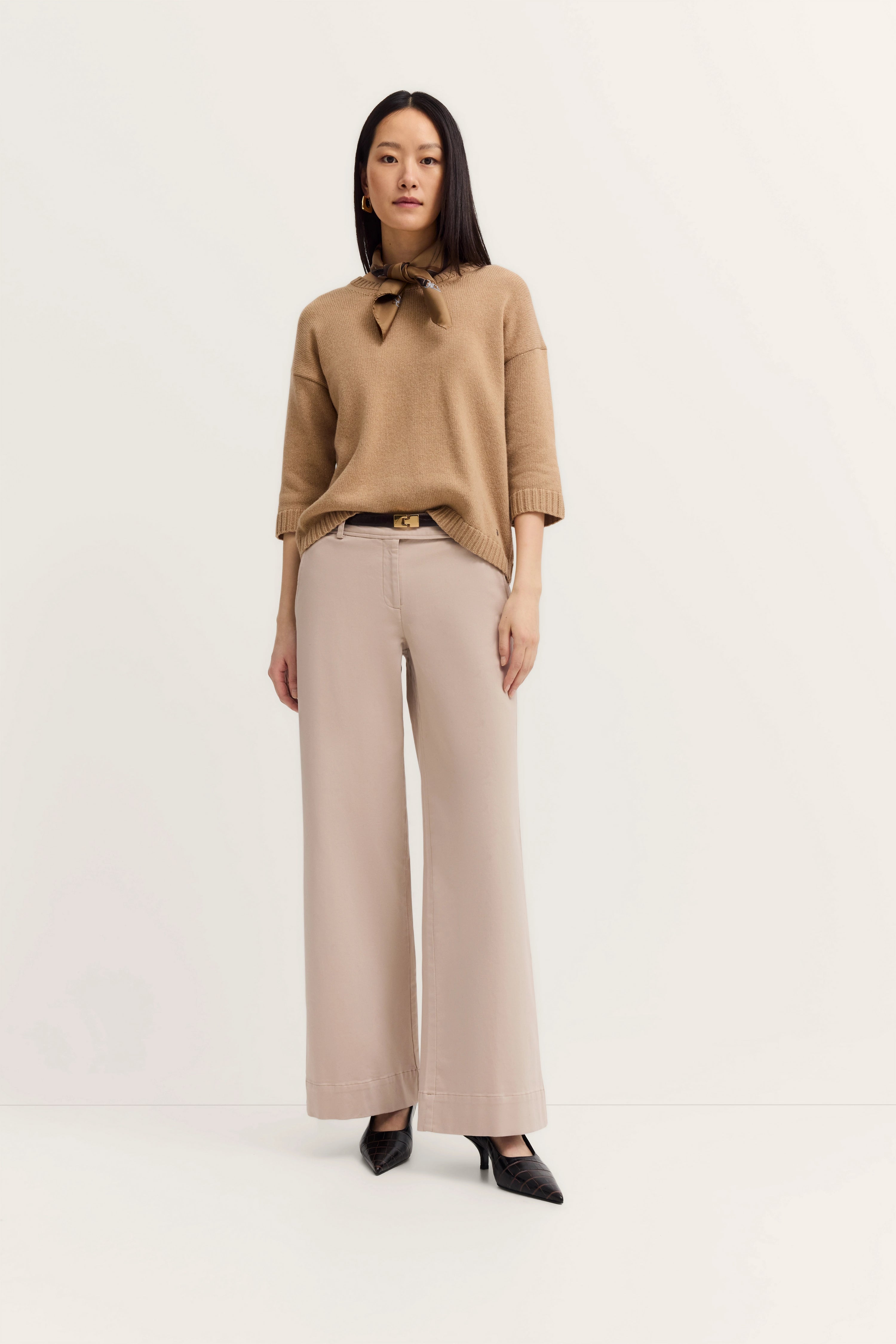 Beige trui, wijde broek, zwarte riem, model poseert staand, elegant bugatti outfit.