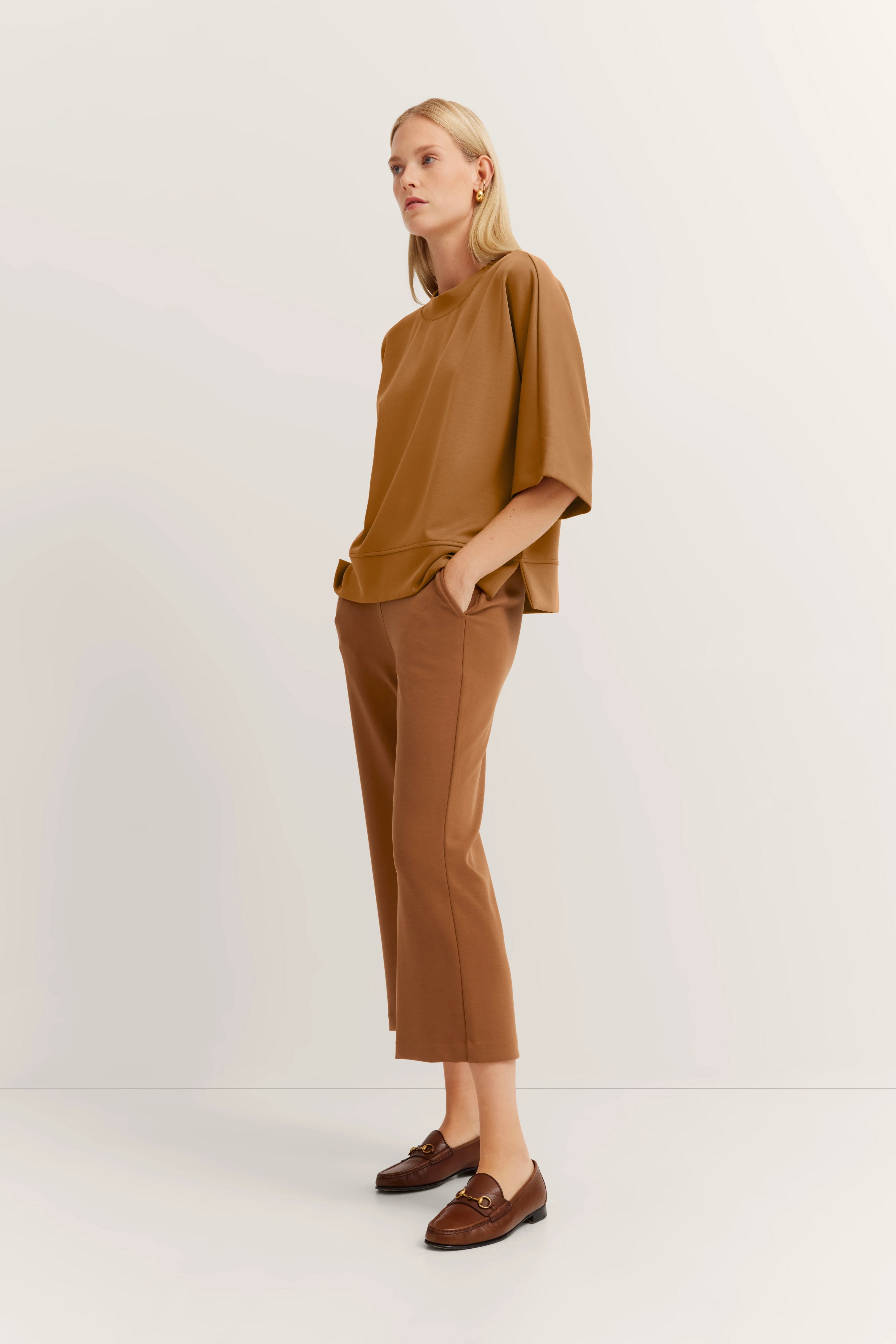 Model in camel outfit met wijde mouwen, bruine broek, bruine loafers