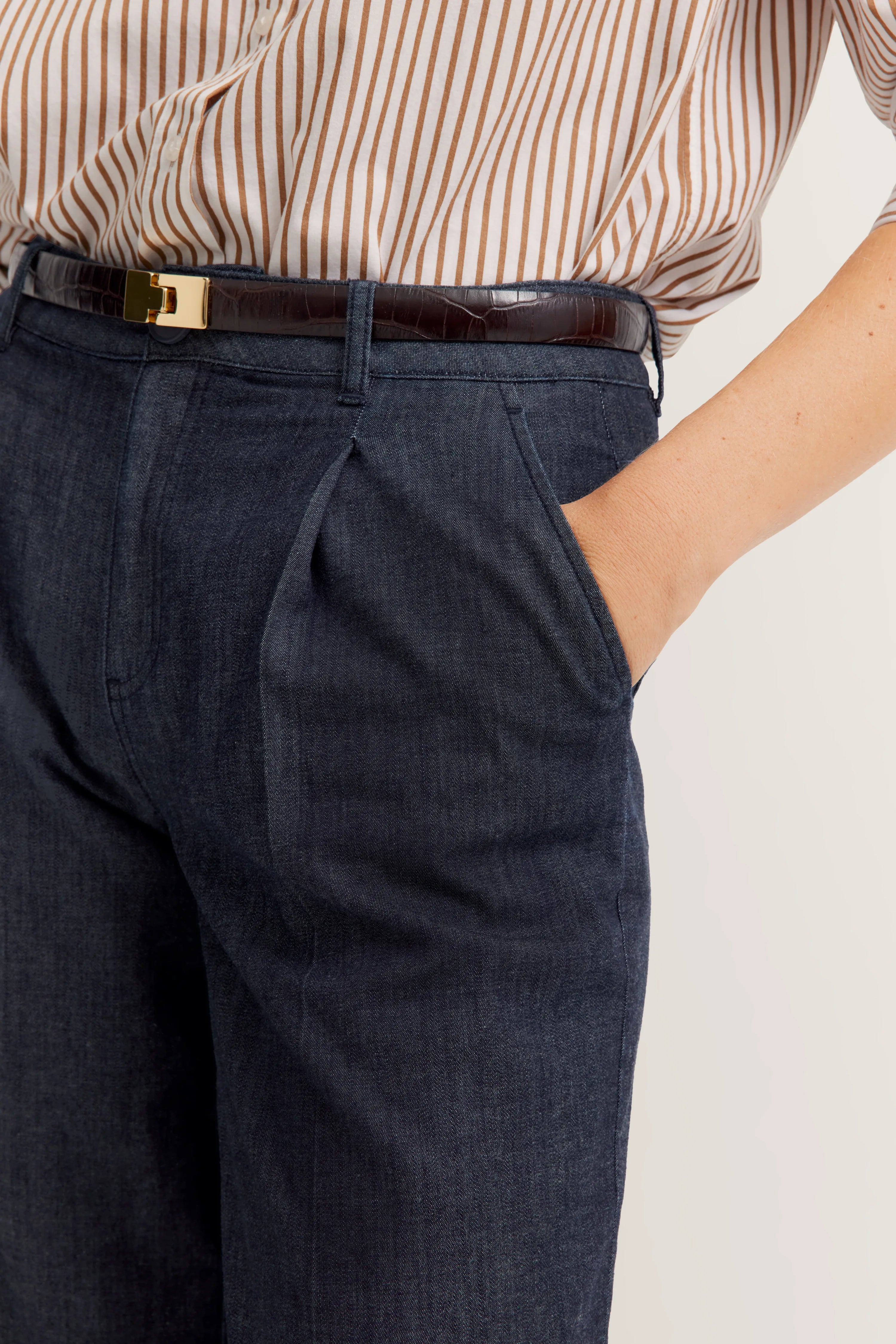Streepblouse in beige-wit met donkerblauwe broek en leren riem, casual busteportret.